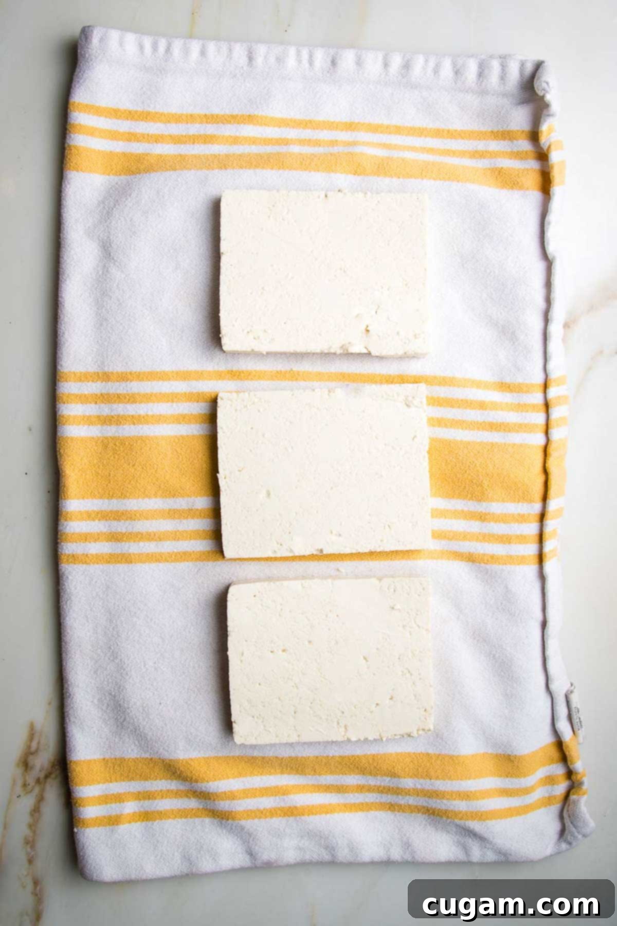 Three slabs of tofu on a kitchen towel. 