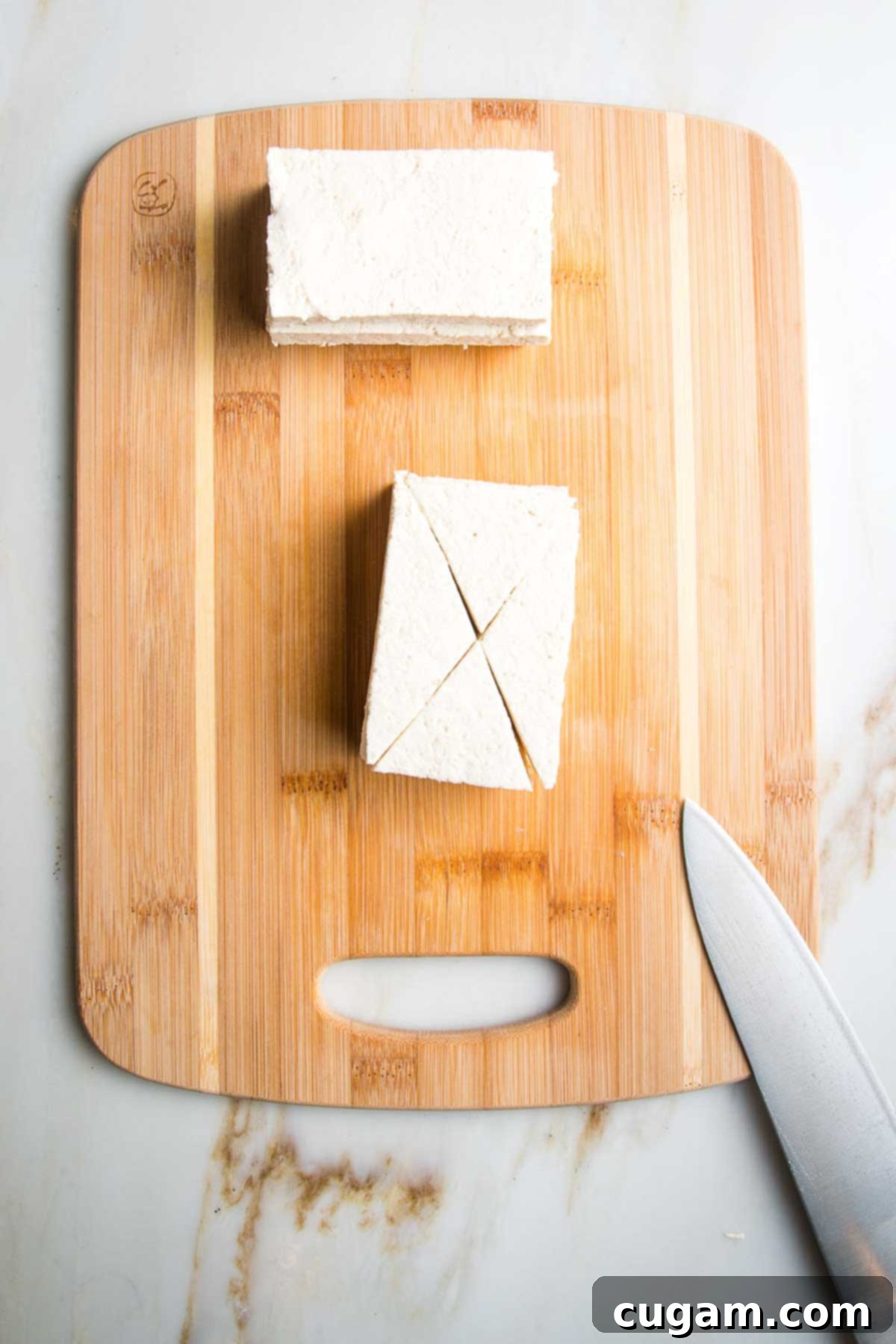Slabs of tofu on a wooden board, being cut into bite sized triangular pieces. 