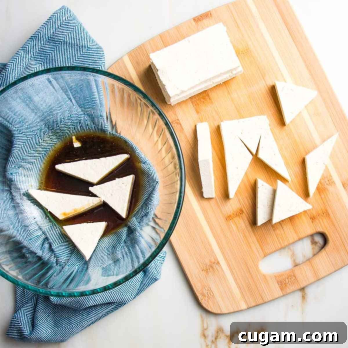 Cutting small pieces of tofu on a cutting board and then dropping into dark colored marinade in a bowl. 