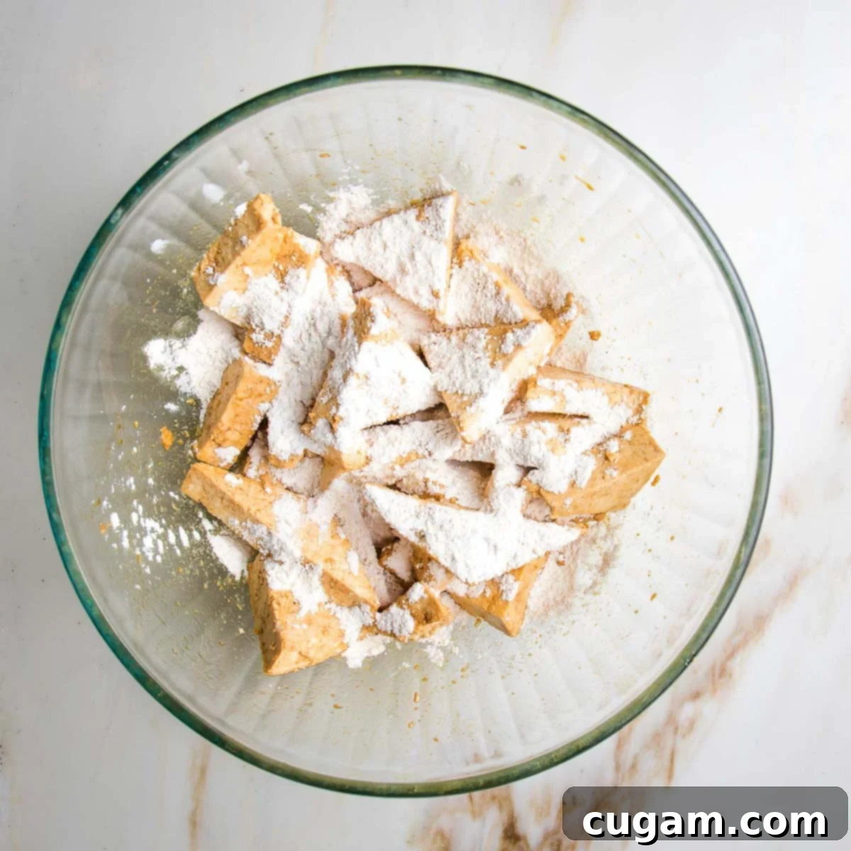 Triangle pieces of tofu in a bowl, sprinkled with white arrowroot powder.