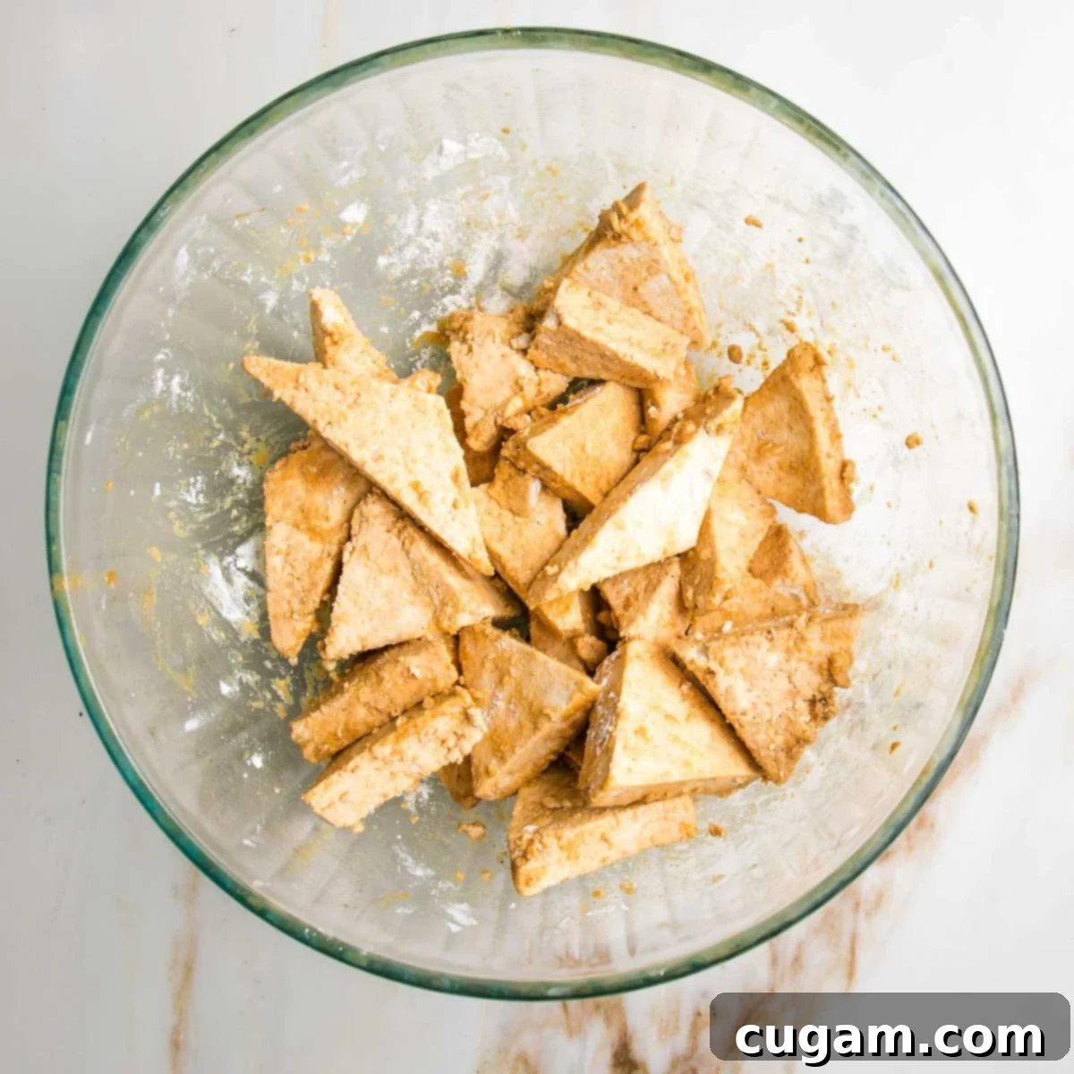 Small, triangle pieces of tofu with marinade and arrowroot in a bowl..