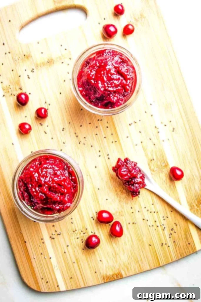 Two small glass jars with cranberry jam, a few cranberries on the sides plus a spoonful of jam.