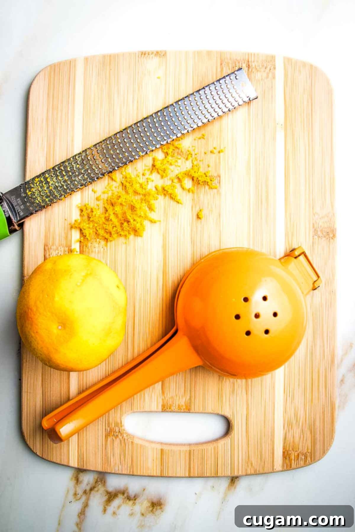Whole orange that has been zested with a microplane onto a cutting board and a citrus juicer on the side.