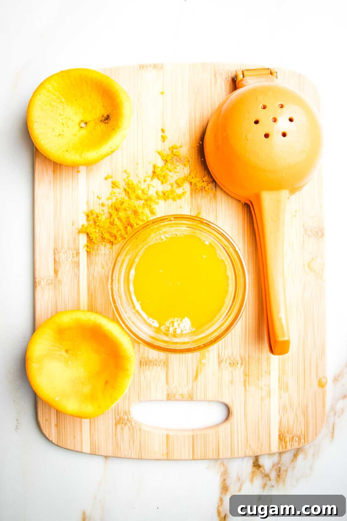 Orange that's been zested and juiced, the squished orange halves still on the cutting board along with the juicer, a dish of the juice and zest on the cutting board.