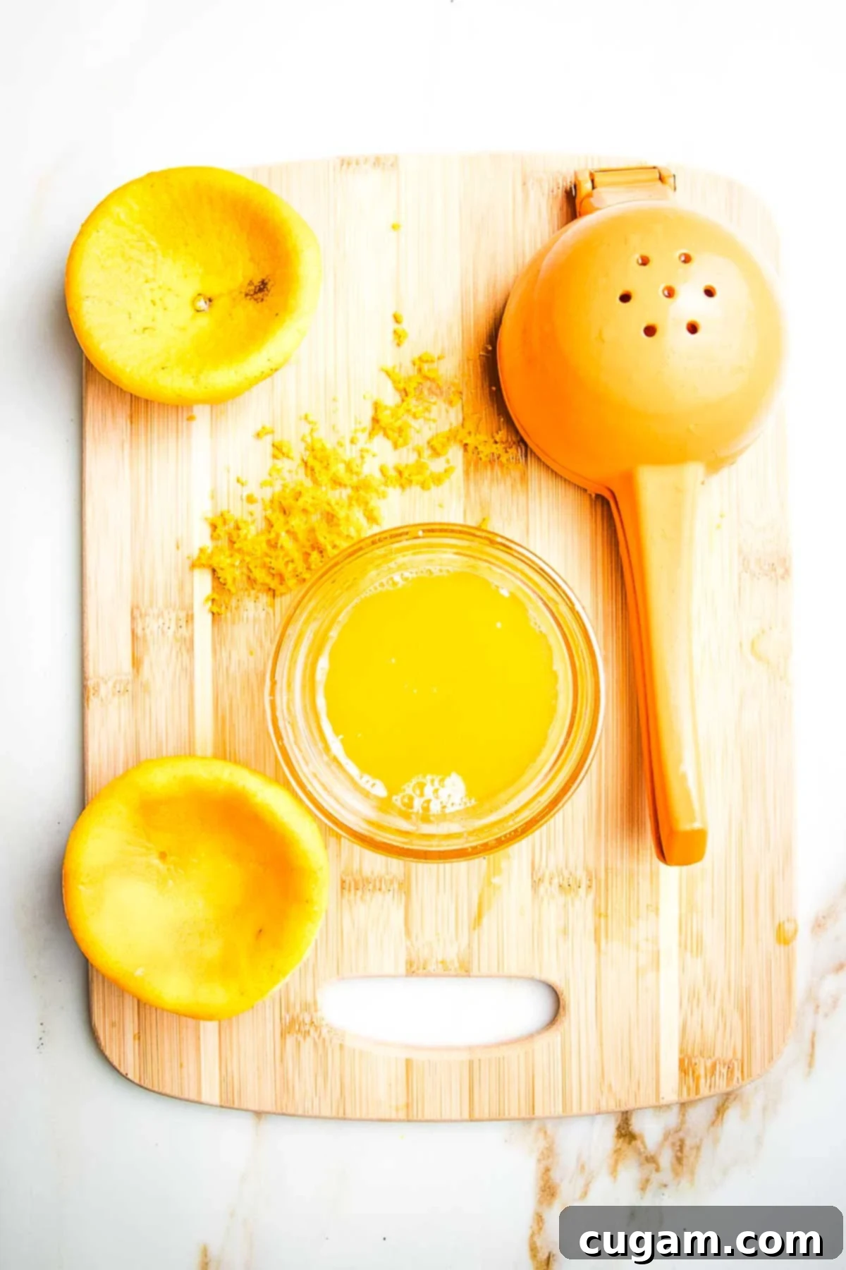 Orange that's been zested and juiced, the squished orange halves still on the cutting board along with the juicer, a dish of the juice and zest on the cutting board.