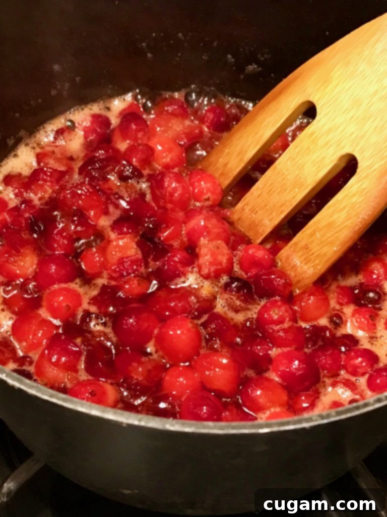 Saucepan with cranberries foaming as they cook, a wooden spatula is stirring them. 