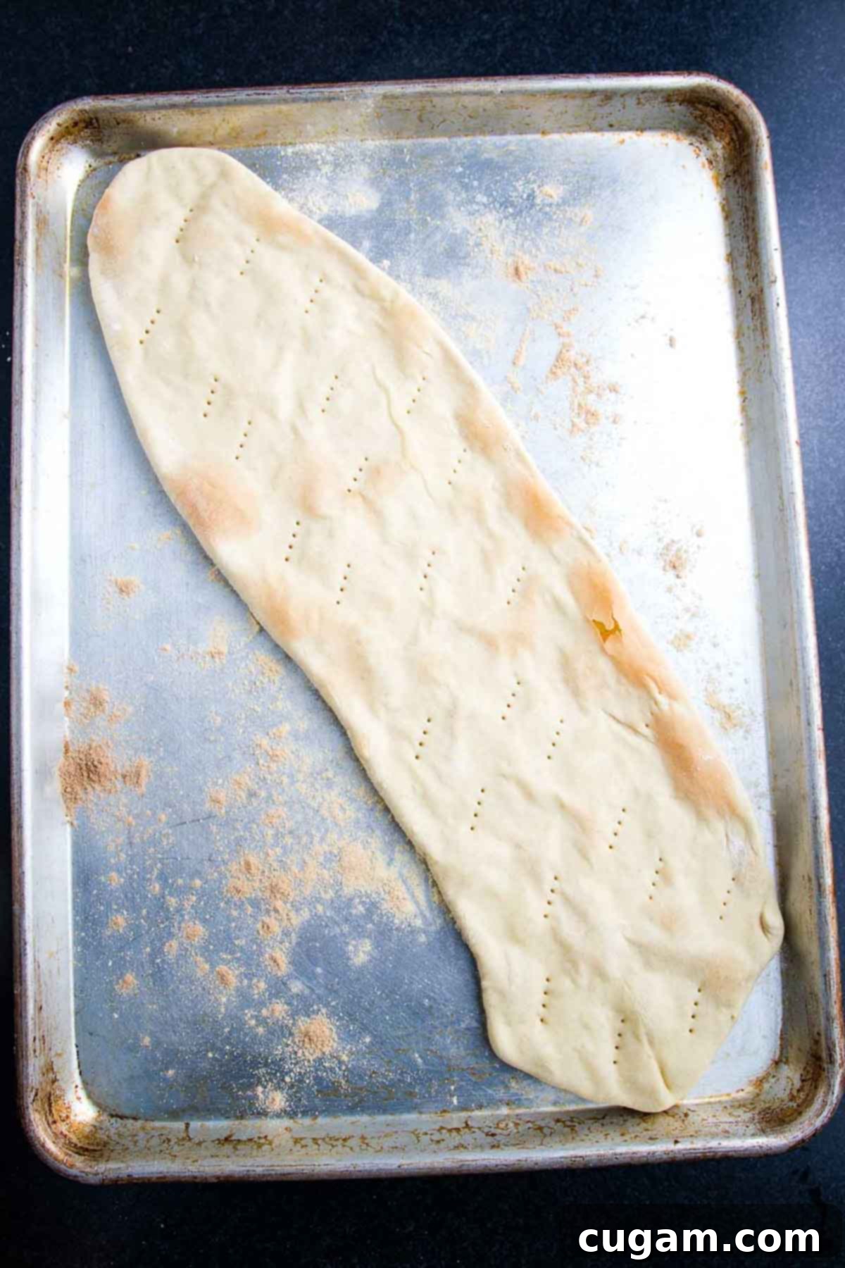 A crisped, par-baked flatbread pizza dough resting on a baking sheet.