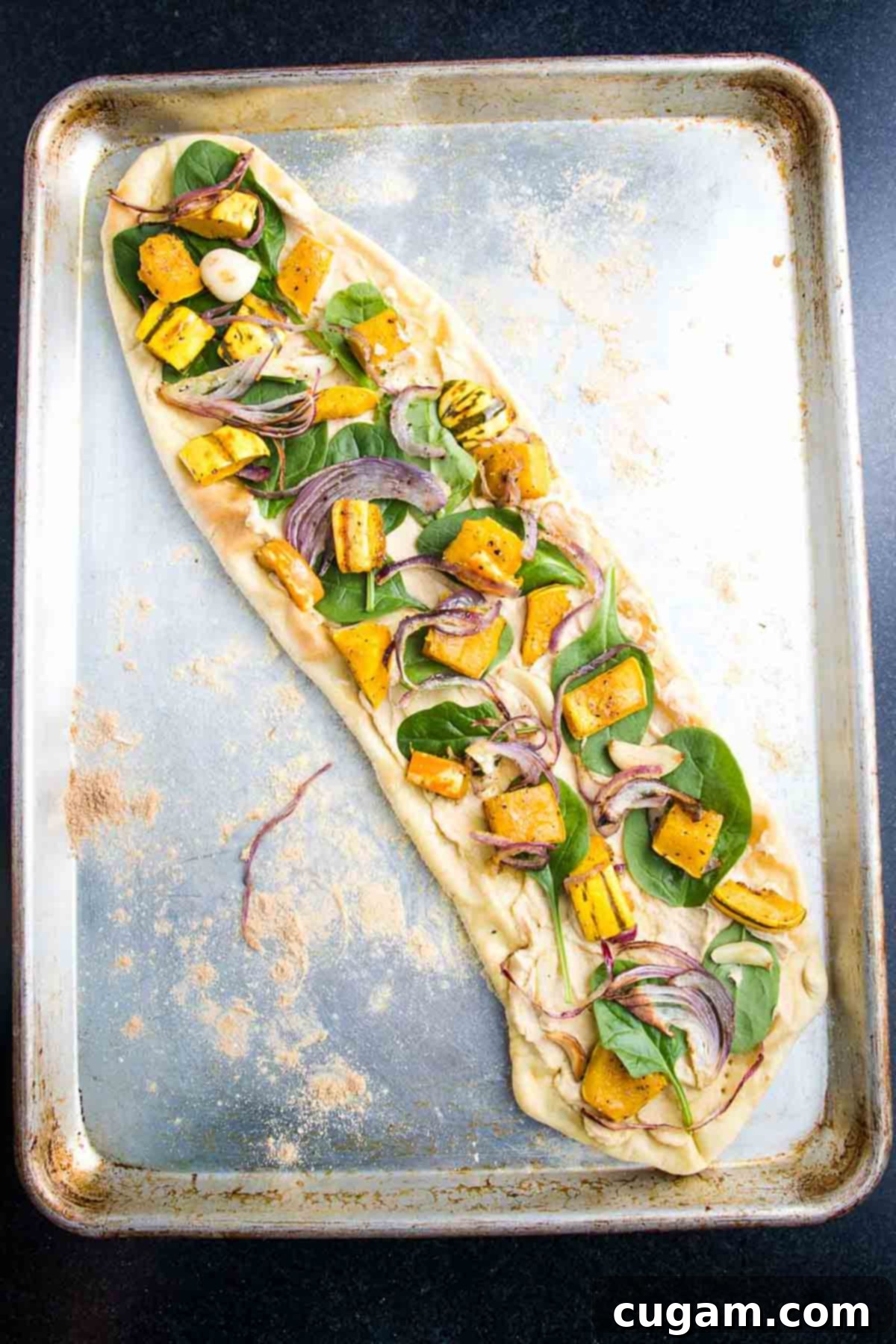 A finished flatbread pizza, topped with roasted delicata squash, caramelized onions, and tender garlic.