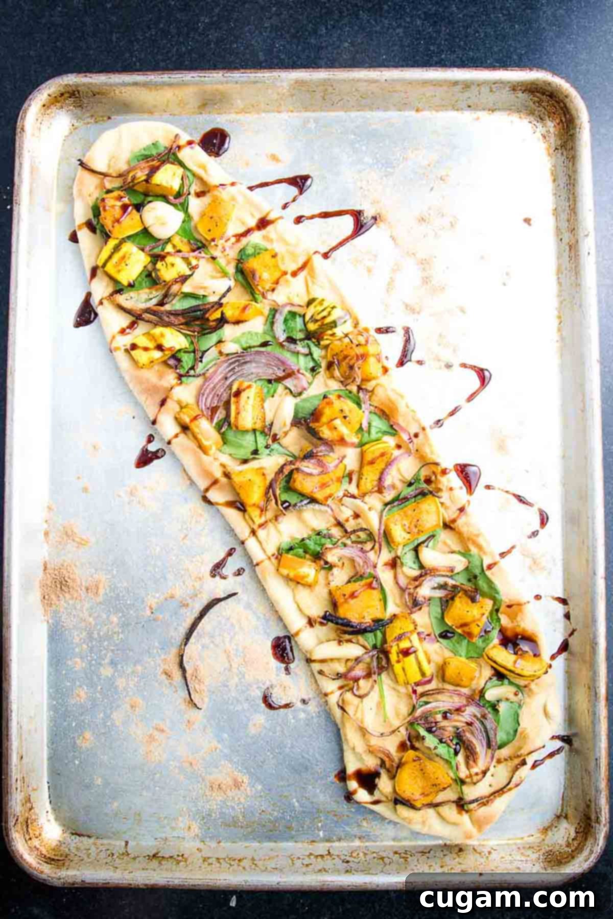 A flatbread pizza, spread with hummus, topped with spinach and roasted squash, and elegantly drizzled with date syrup.