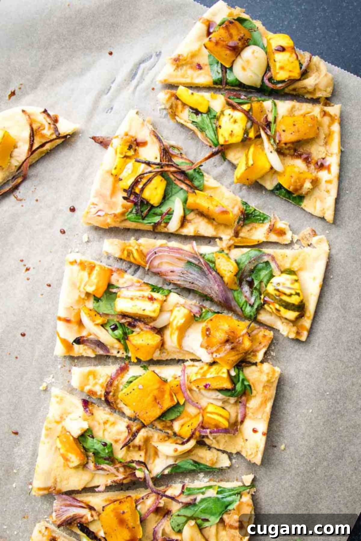 A vegan flatbread pizza, topped with roasted squash, onions, and garlic, cut into small triangle slices, ready to be served.