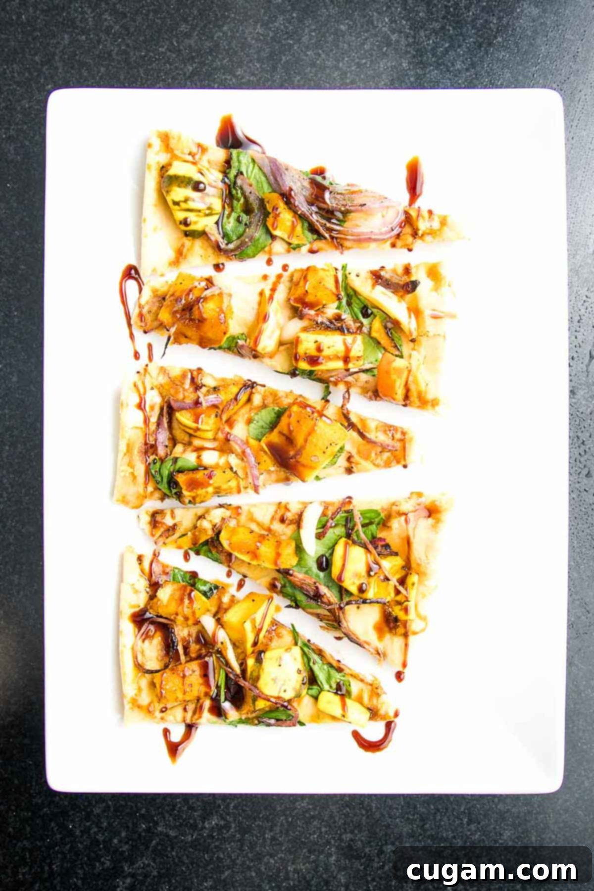 Slices of vegan flatbread, artfully topped with creamy hummus, roasted vegetables, and a delicate drizzle of date syrup, arranged for serving.
