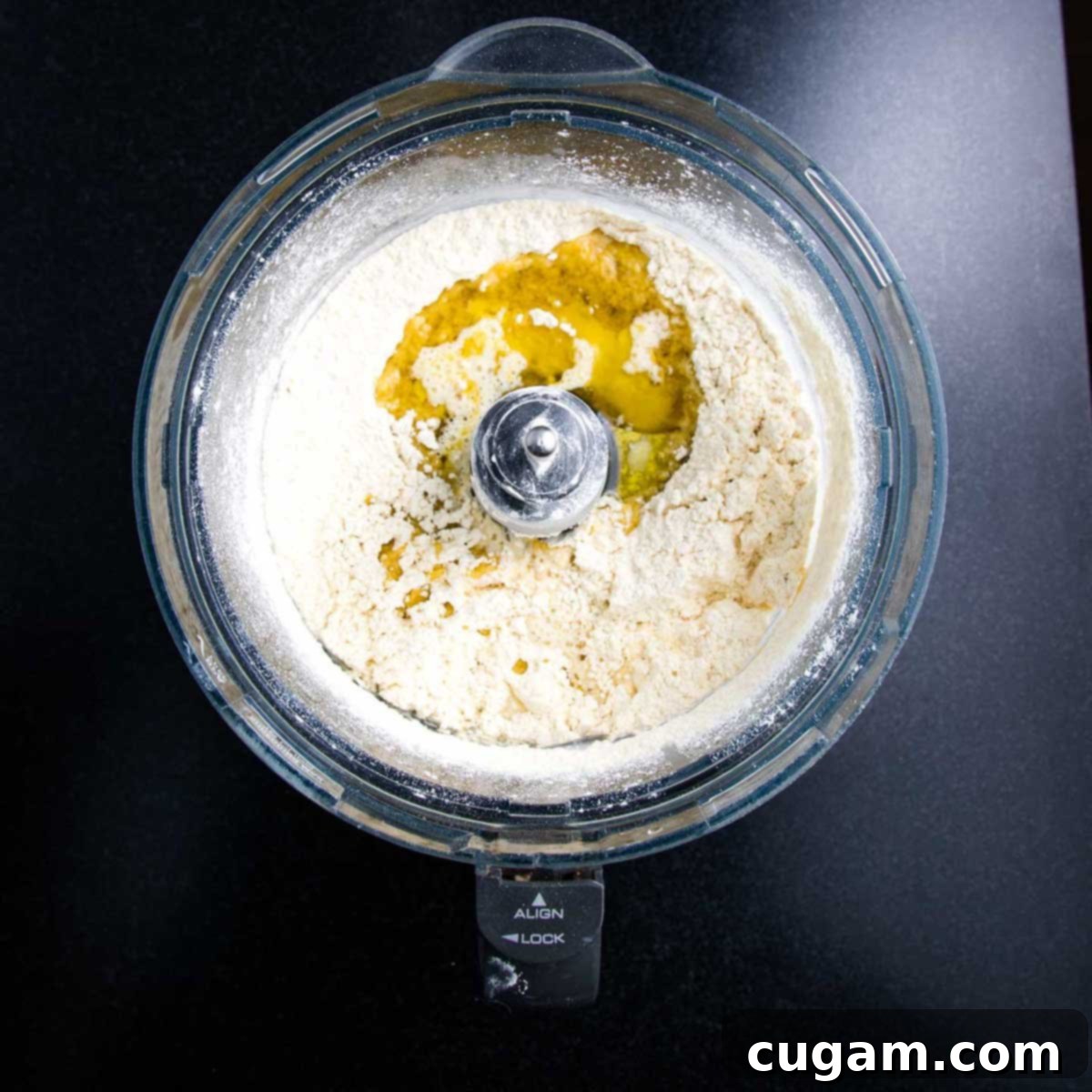 Olive oil and warm water are poured into a food processor bowl containing flour and salt.