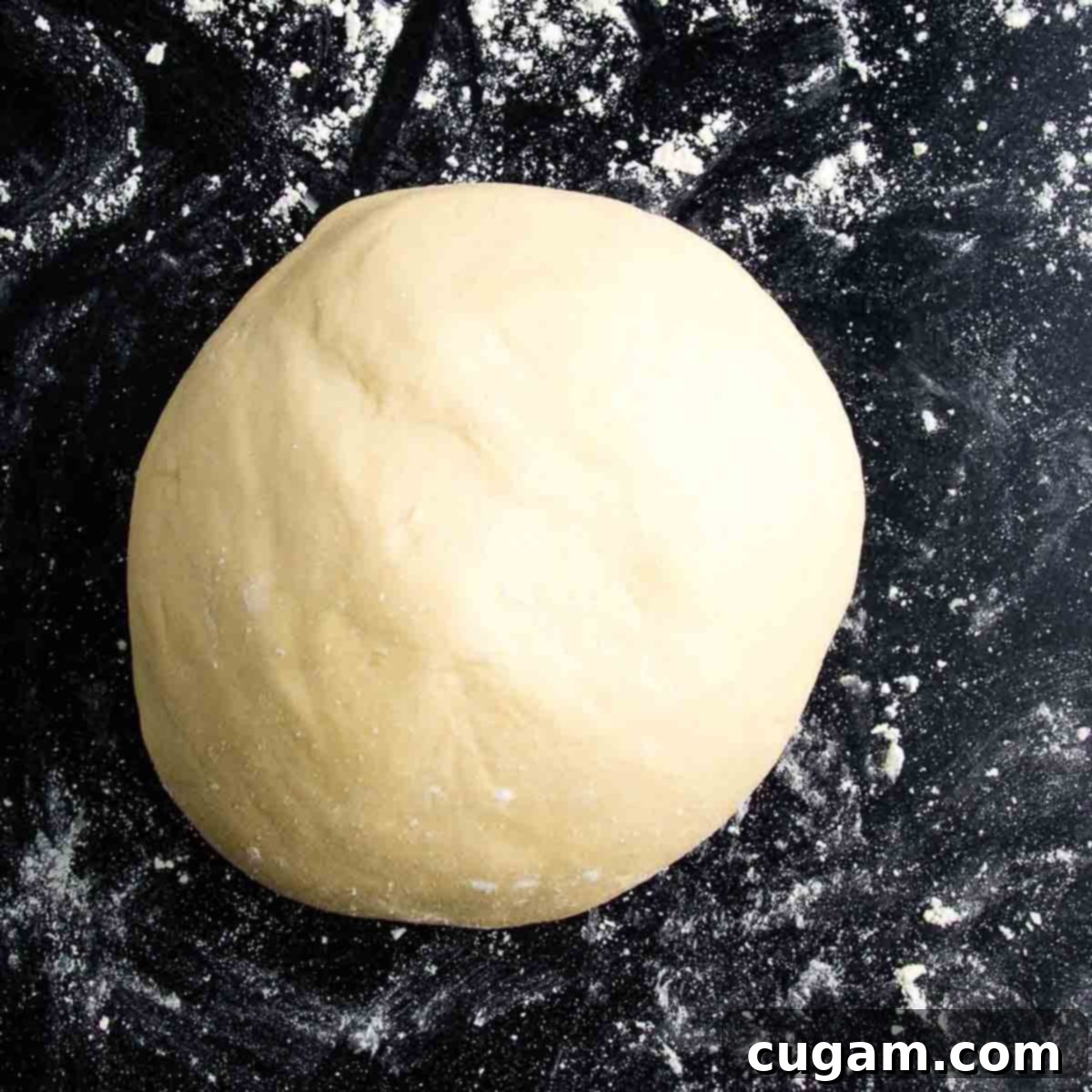 Smooth ball of flatbread dough resting on a floured black surface.