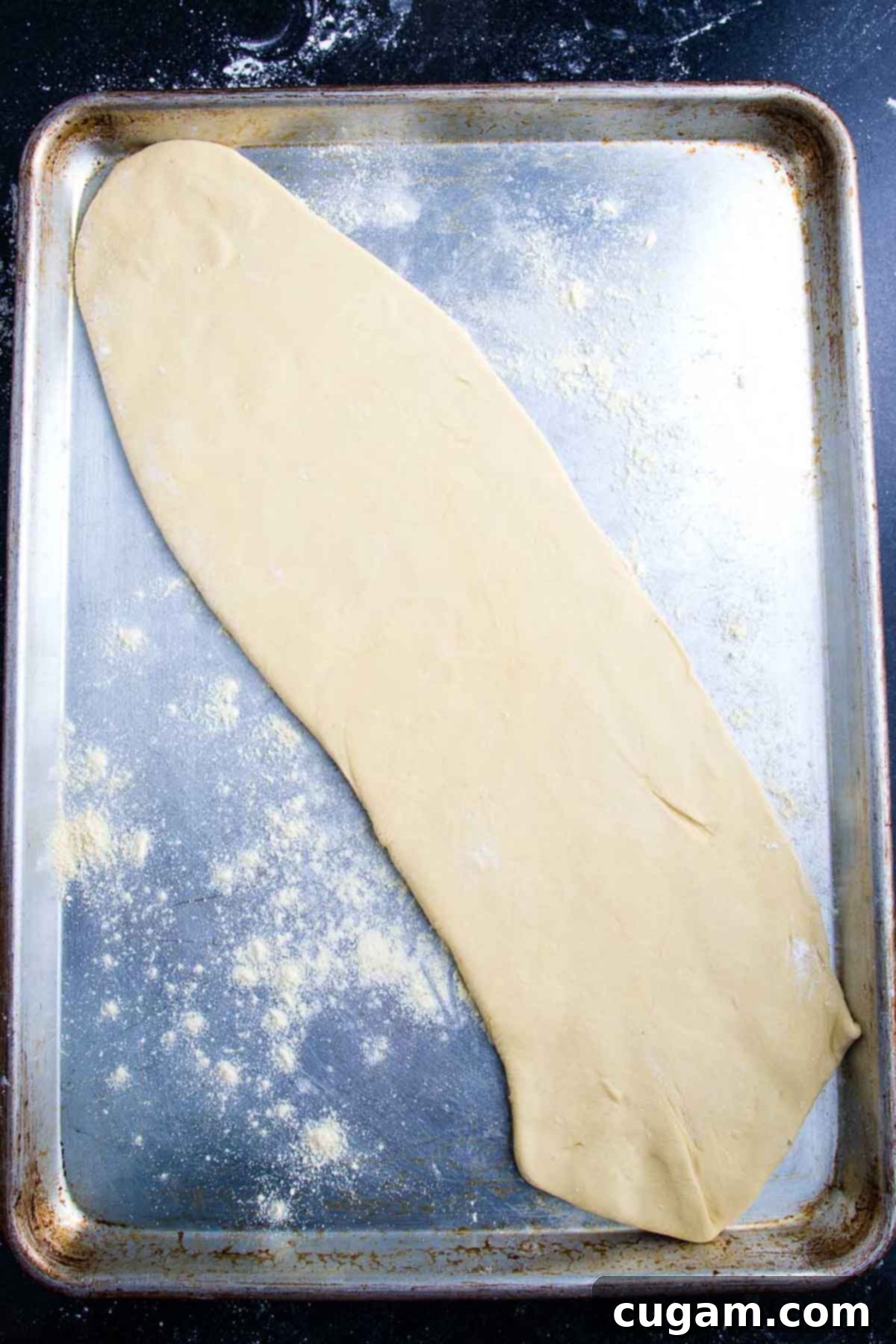 A thinly rolled out oval of pizza dough is carefully placed on a rimmed baking tray.