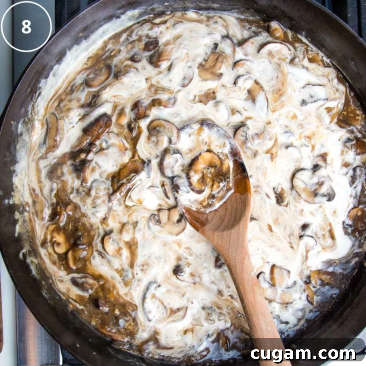 Vegan sour cream being gently stirred into the rich mushroom sauce in a cast iron skillet, creating a creamy texture.