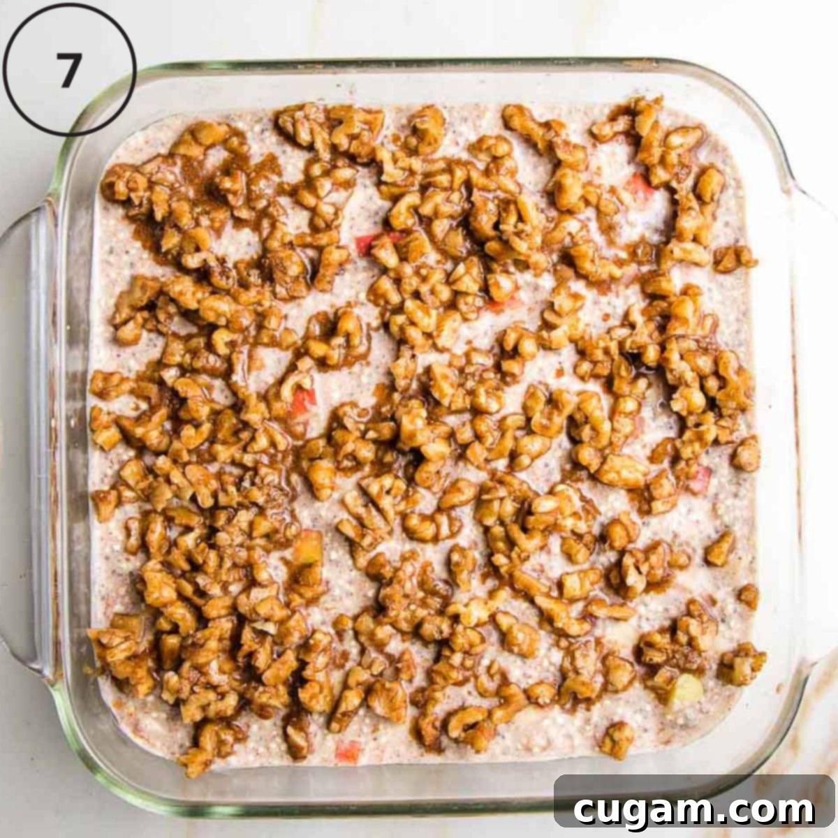 A square glass baking dish filled with the quinoa batter, now generously topped with the spiced nut mixture, creating a rustic and inviting appearance before baking.