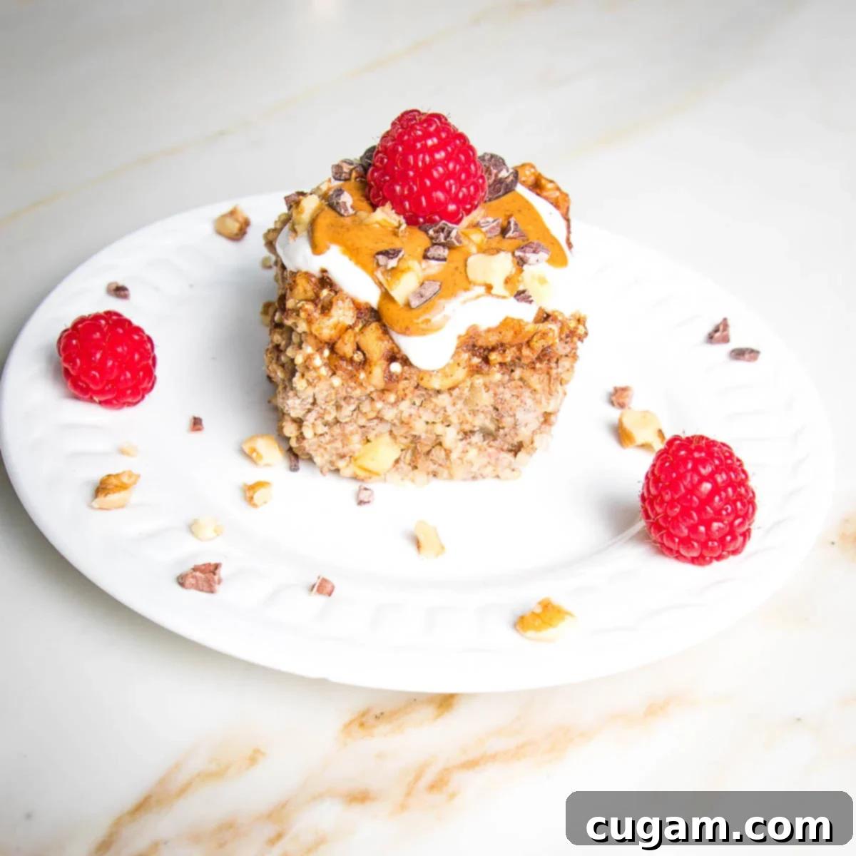 A charming plate holding a perfect square of baked quinoa, elegantly topped with a silky drizzle of almond butter, a dollop of creamy plant-based yogurt, and a handful of fresh, glistening berries, making for an irresistible and nutritious meal.