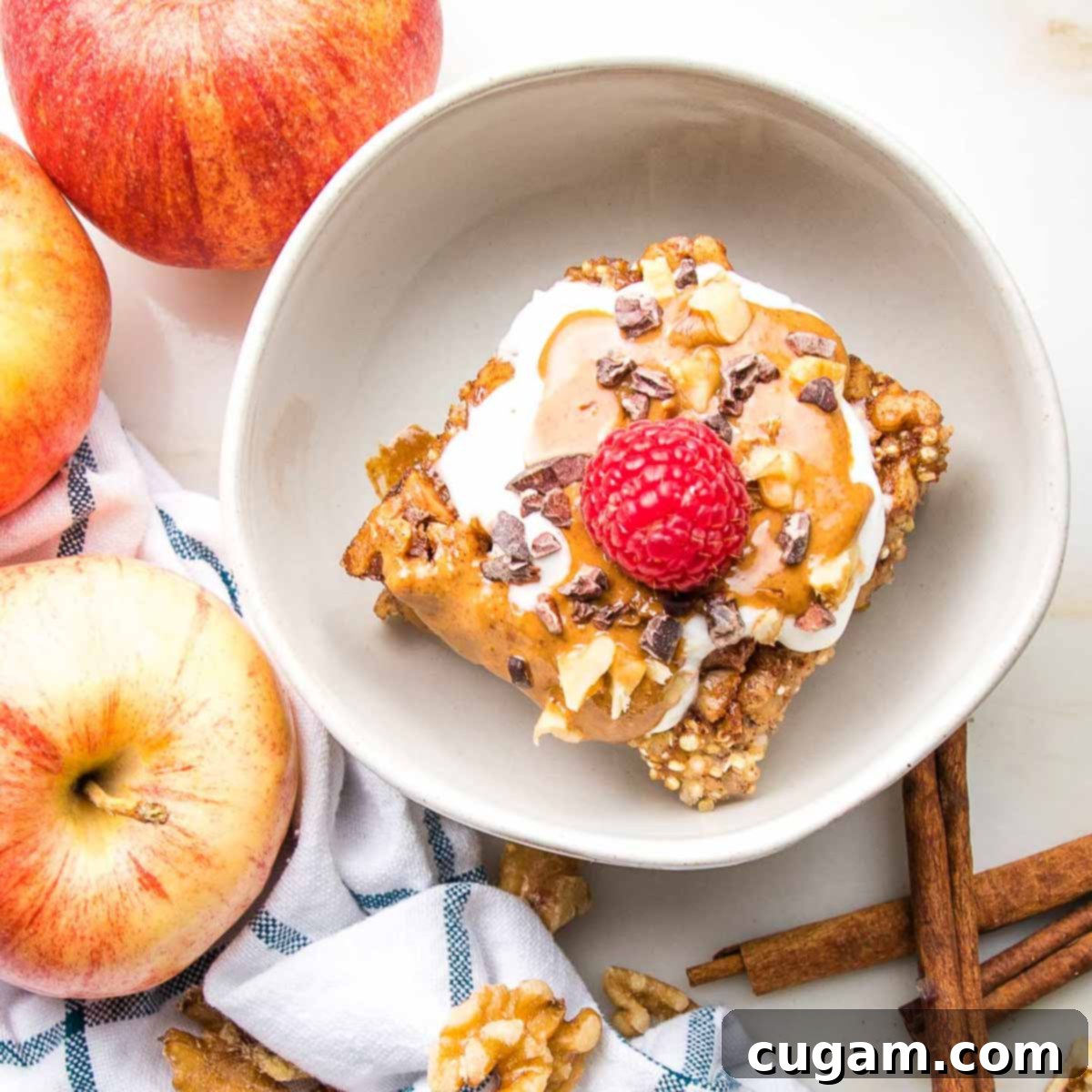 A perfectly portioned square of Quinoa Breakfast Bake, beautifully drizzled with rich peanut butter, topped with a spoonful of creamy yogurt and a vibrant red raspberry, showcasing its deliciousness.