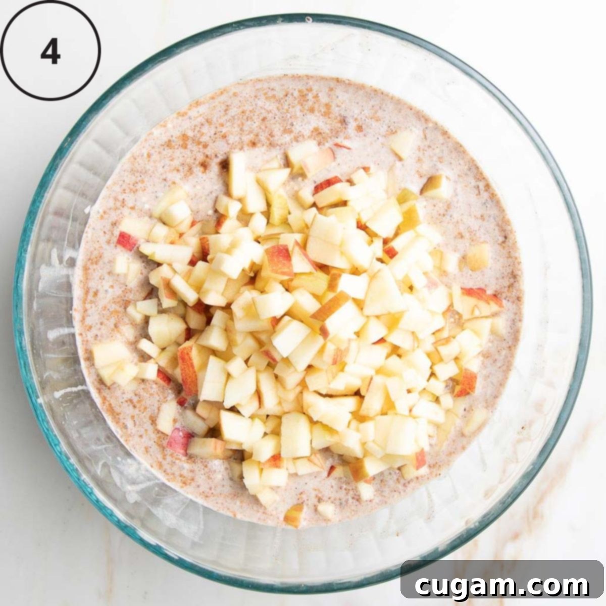 A textured, lumpy batter in a mixing bowl, now with freshly chopped apples, skin still on, carefully stirred in, adding a burst of freshness and natural sweetness.