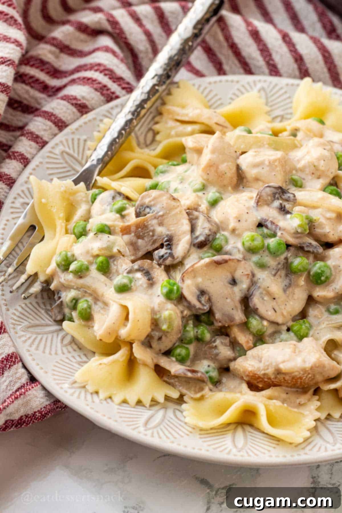 Cooked Chicken Mushroom Stroganoff with creamy sauce, served on a white plate with a fork, garnished with fresh parsley.