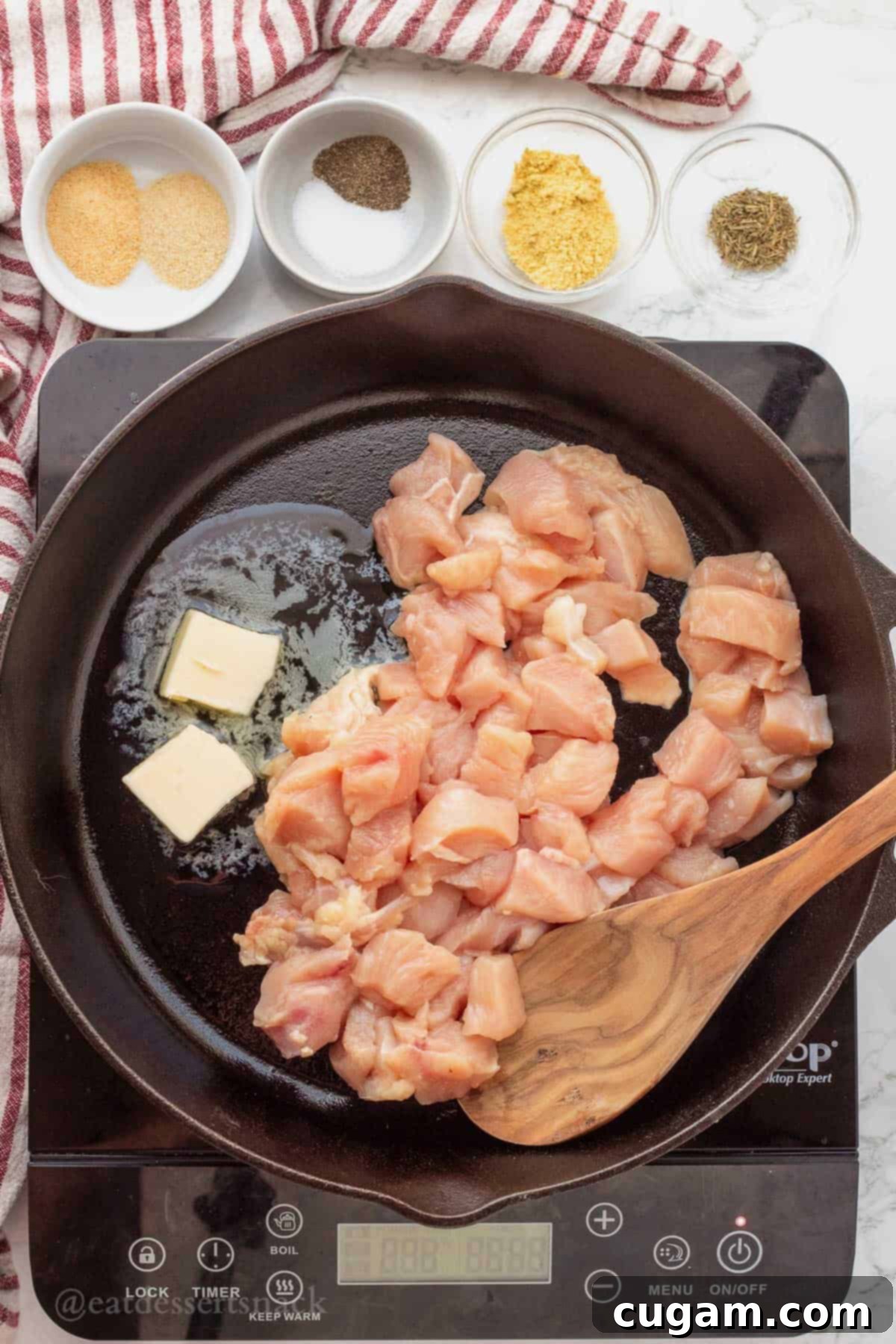 Diced raw chicken cooking in melted butter in a black frying pan, stirred with a wooden spoon.
