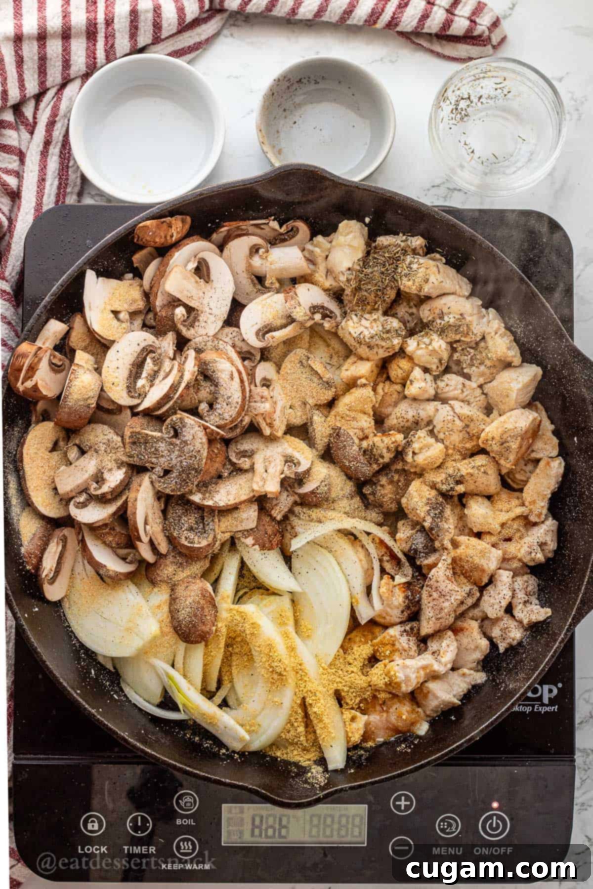 Cooked chicken with raw sliced mushrooms, onions, and spices being added to a black frying pan.