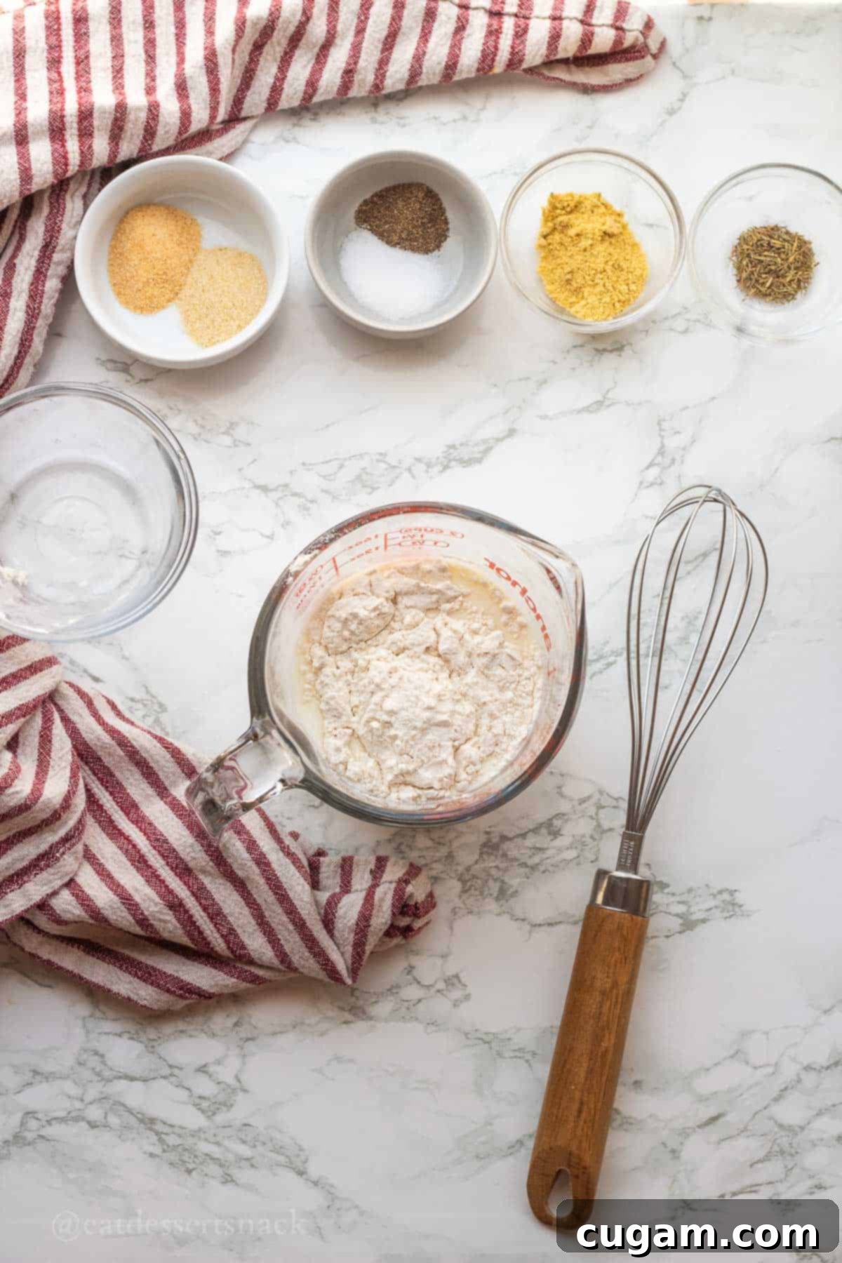 Measuring cup with milk and flour being whisked together on a marble countertop, creating a smooth slurry.