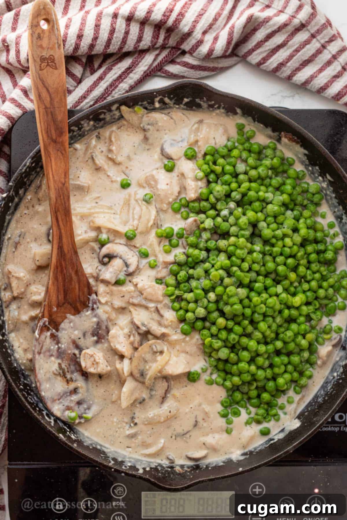 Black frying pan filled with chicken mushroom stroganoff, with frozen peas sprinkled on top, ready for simmering.