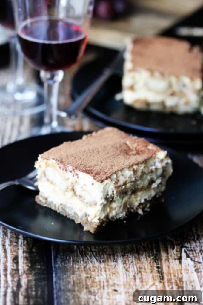 A slice of classic Tiramisu on a plate, with a glass of Italian dessert wine blurred in the background, suggesting a perfect pairing.