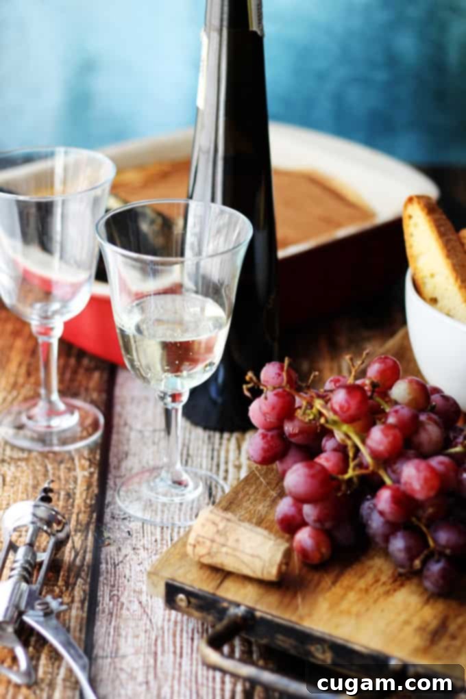 A clear glass of Moscato d'Asti, light in color and slightly effervescent, surrounded by fresh grapes and small Italian pastries.