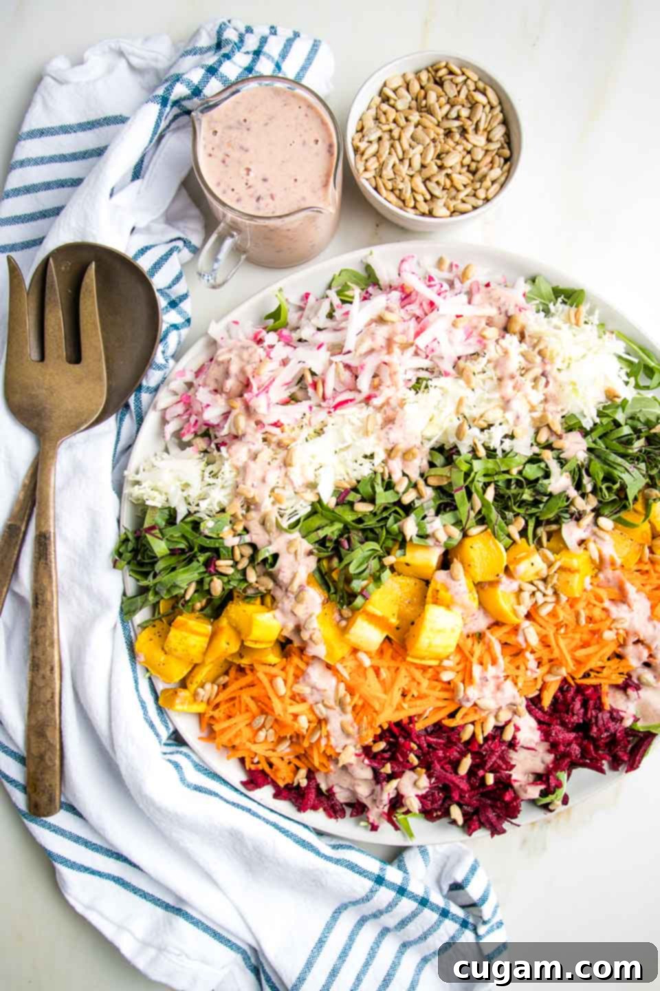 Kaleidoscope Nourish Bowl 2 Shredded Rainbow Salad: radishes, cabbage, beet greens, carrots, red beets and roasted delicata squash cubes on a white rimmed plate, plus a small cut of pink dressing and a bowl of sunflower seeds.