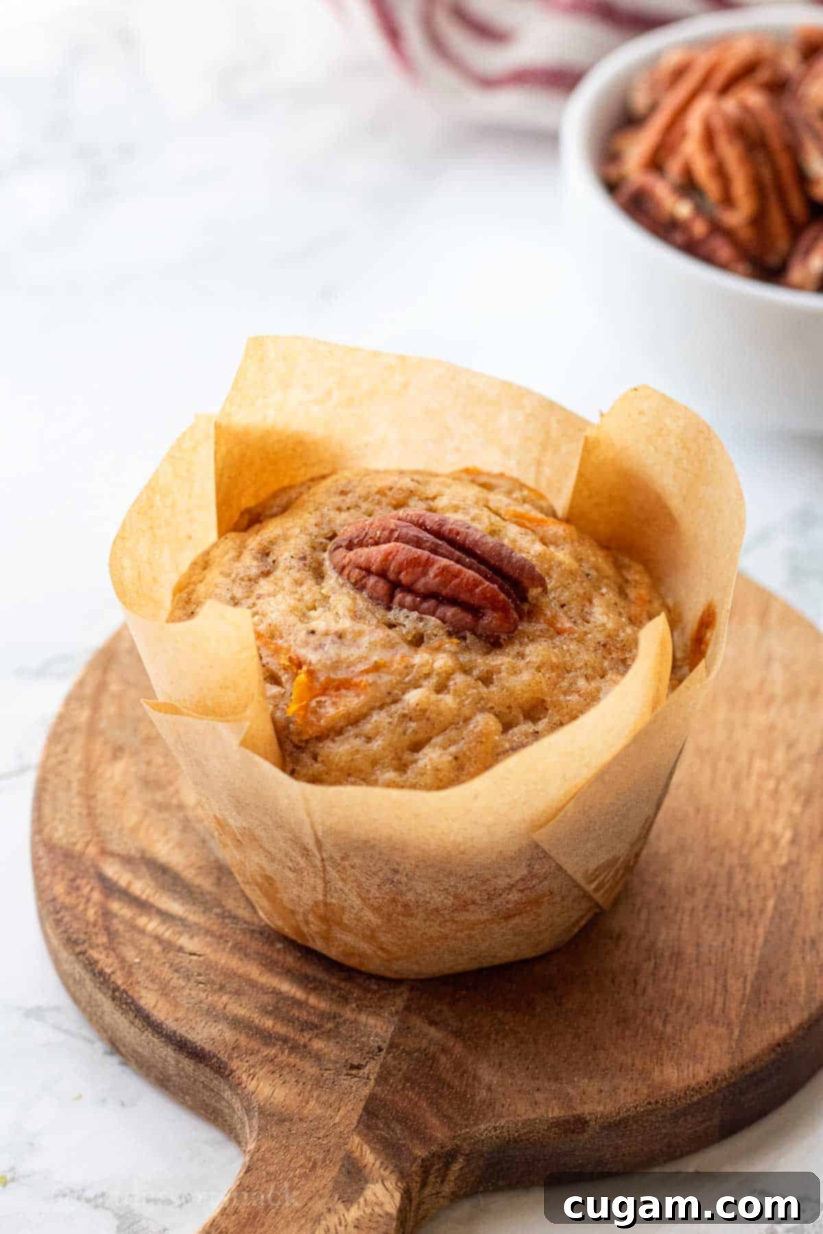Baked banana carrot muffin in brown paper on wood board.