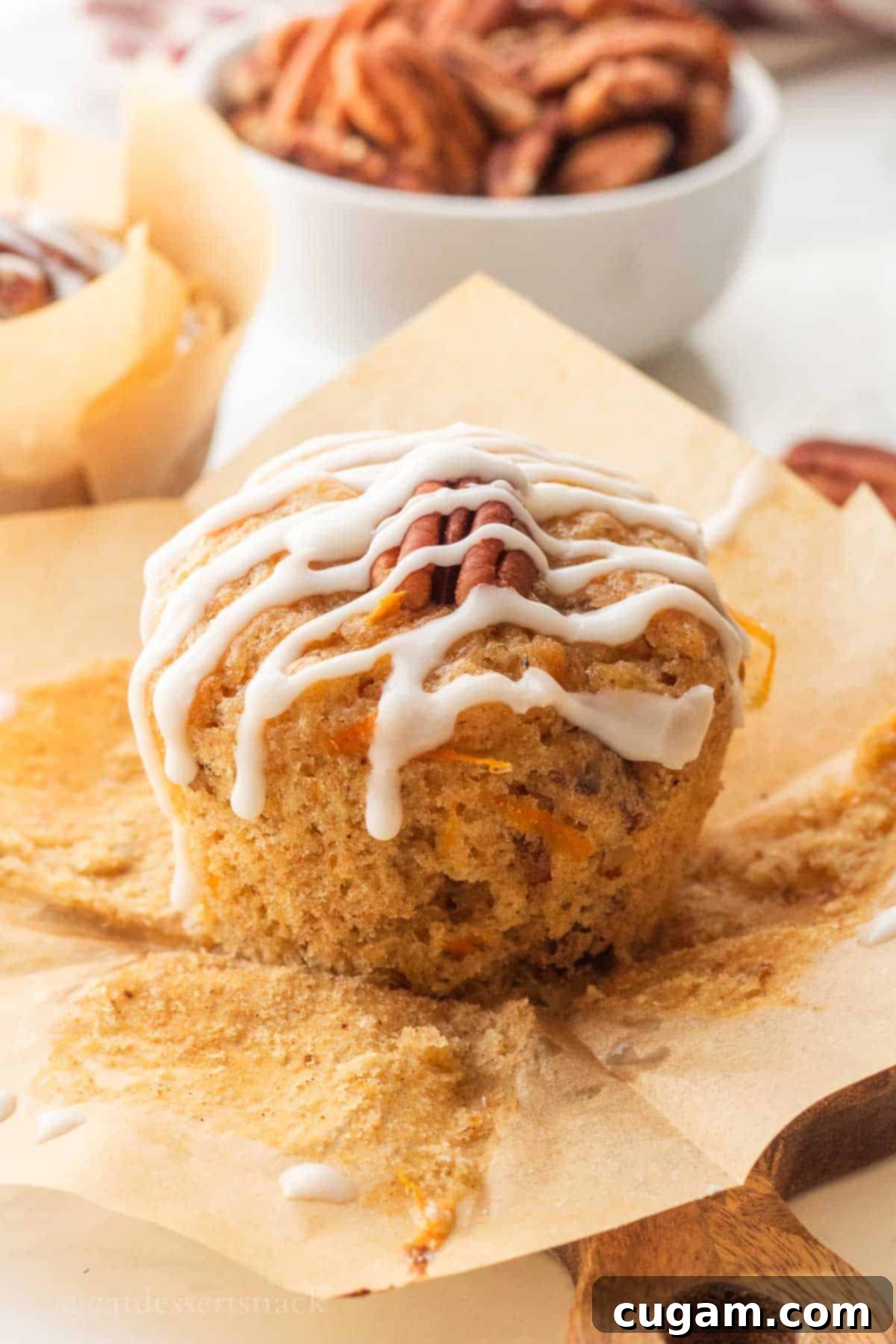 Icing drizzle over baked carrot banana muffin on brown paper.