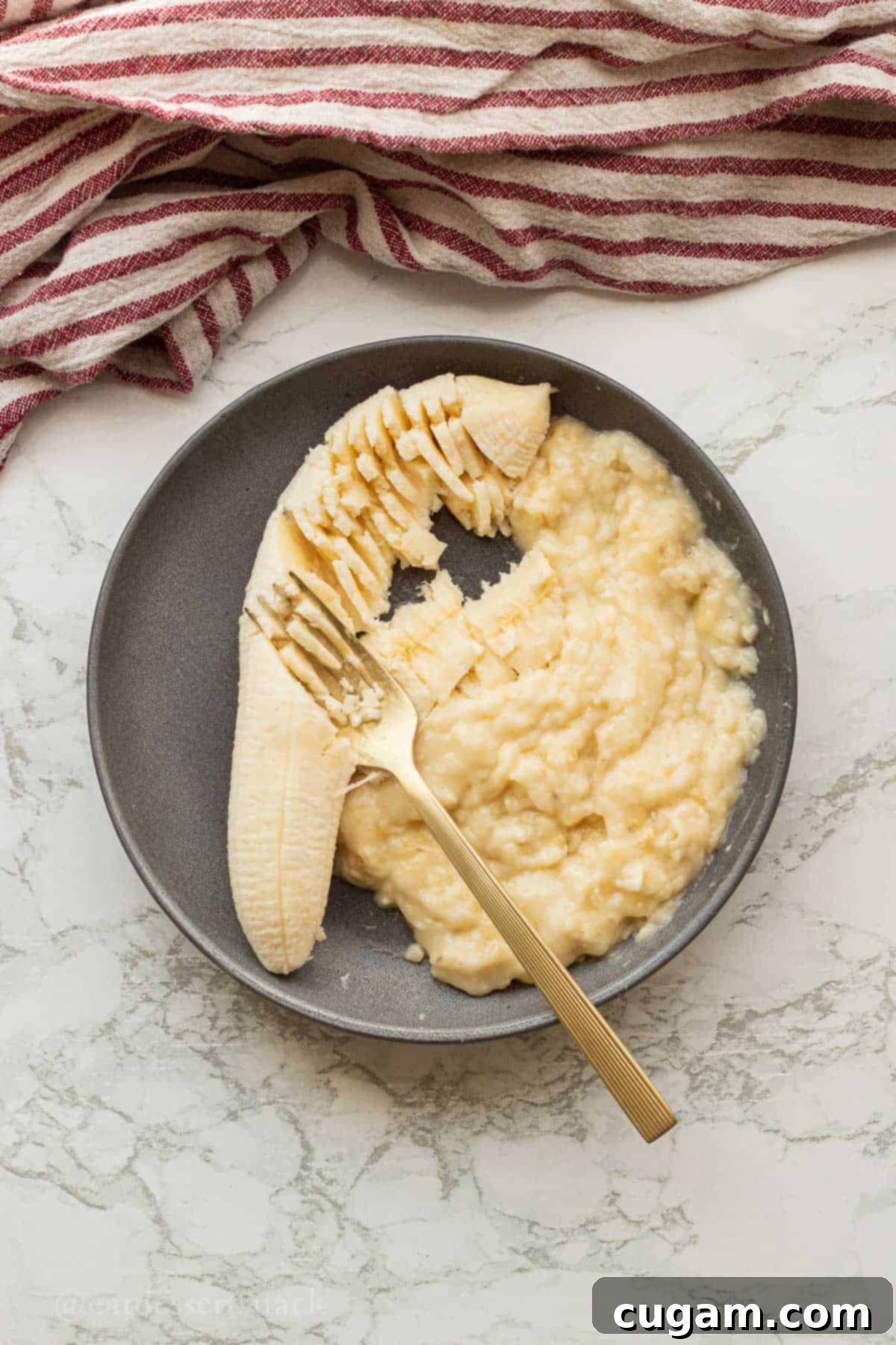 Fork mashing banana in black bowl.