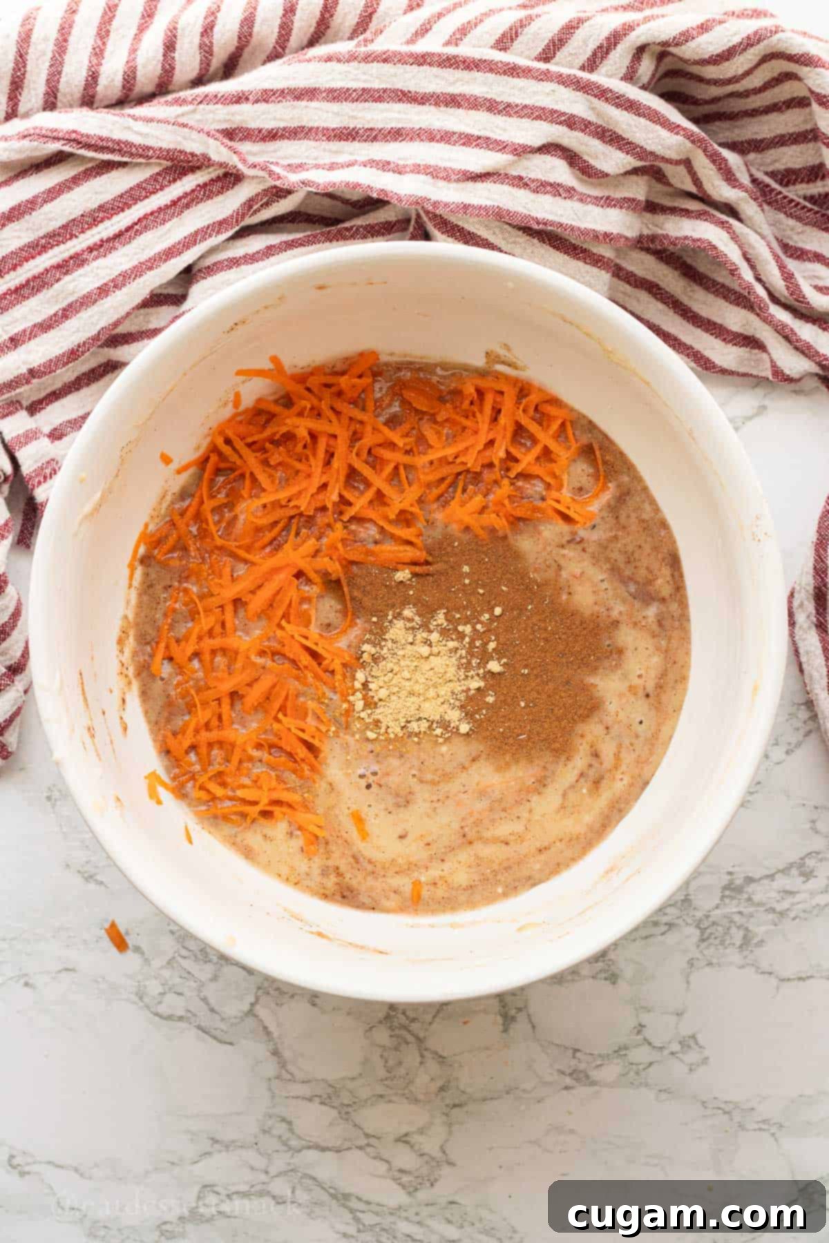 Shredded carrots and spices in white bowl of banana carrot muffin batter.