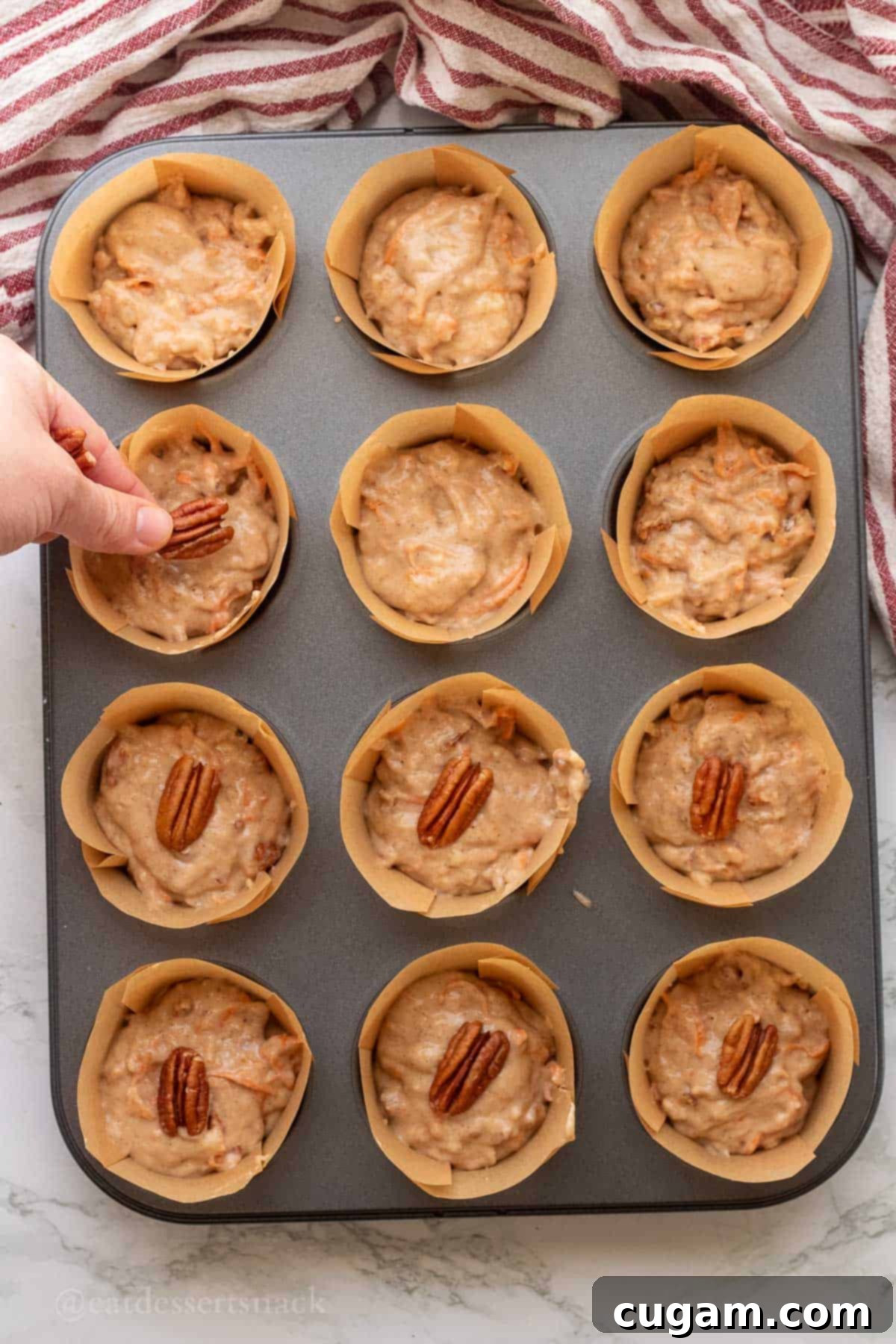 Hand placing pecans on raw muffin batter.