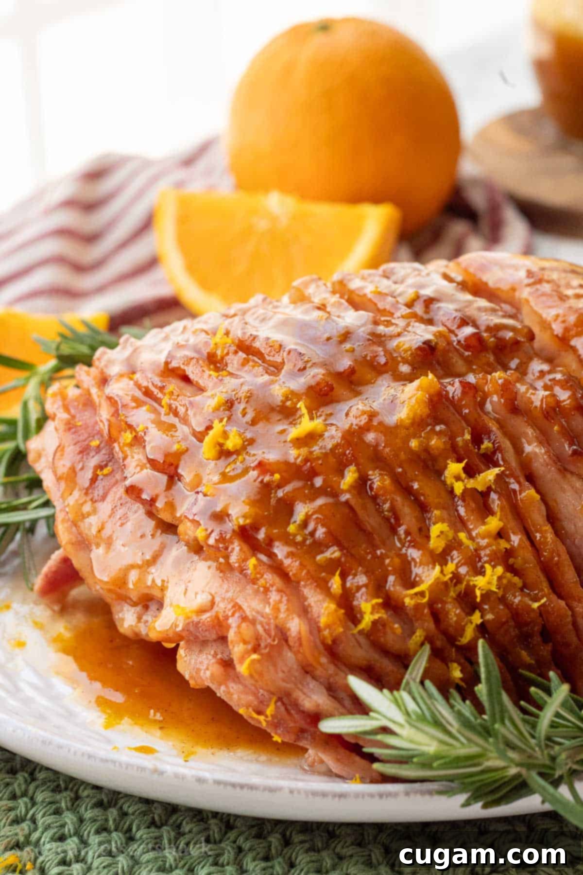 A beautifully orange glazed ham garnished with fresh rosemary on a white platter, ready to be carved and served.