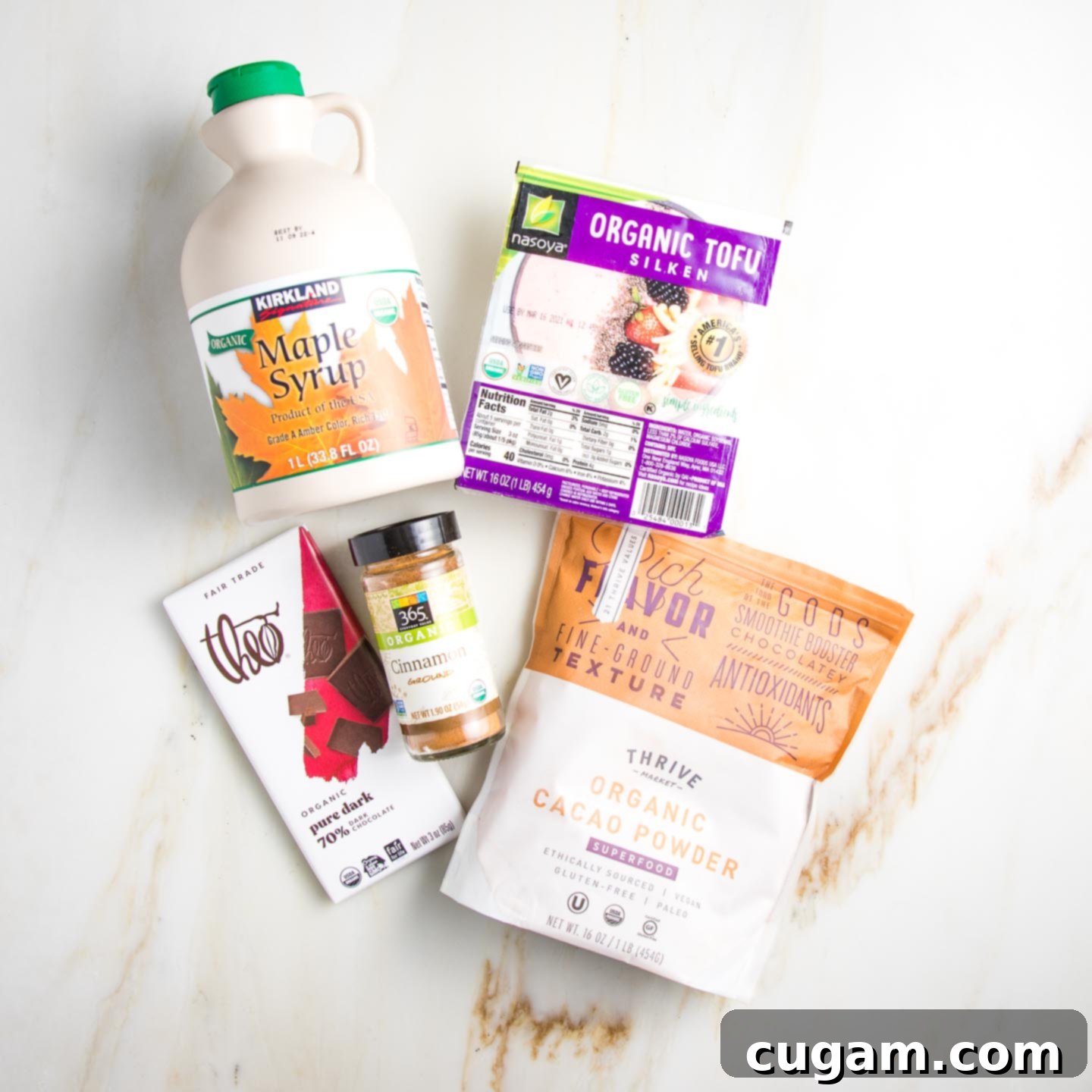 Ingredients on a counter: maple syrup, silken tofu, dark chocolate, cinnamon and cacao powder.