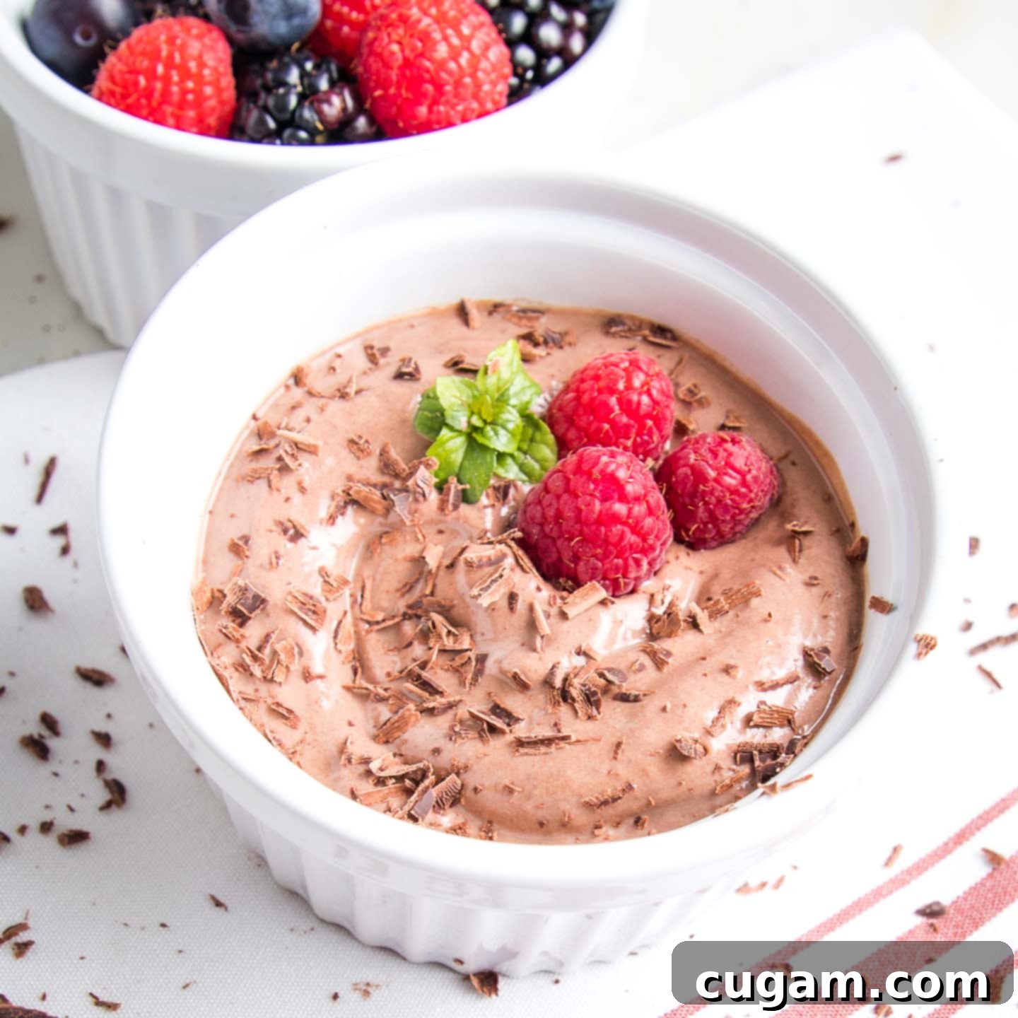 Chocolate pudding in a ramekin with chocolate shavings and raspberries on top.