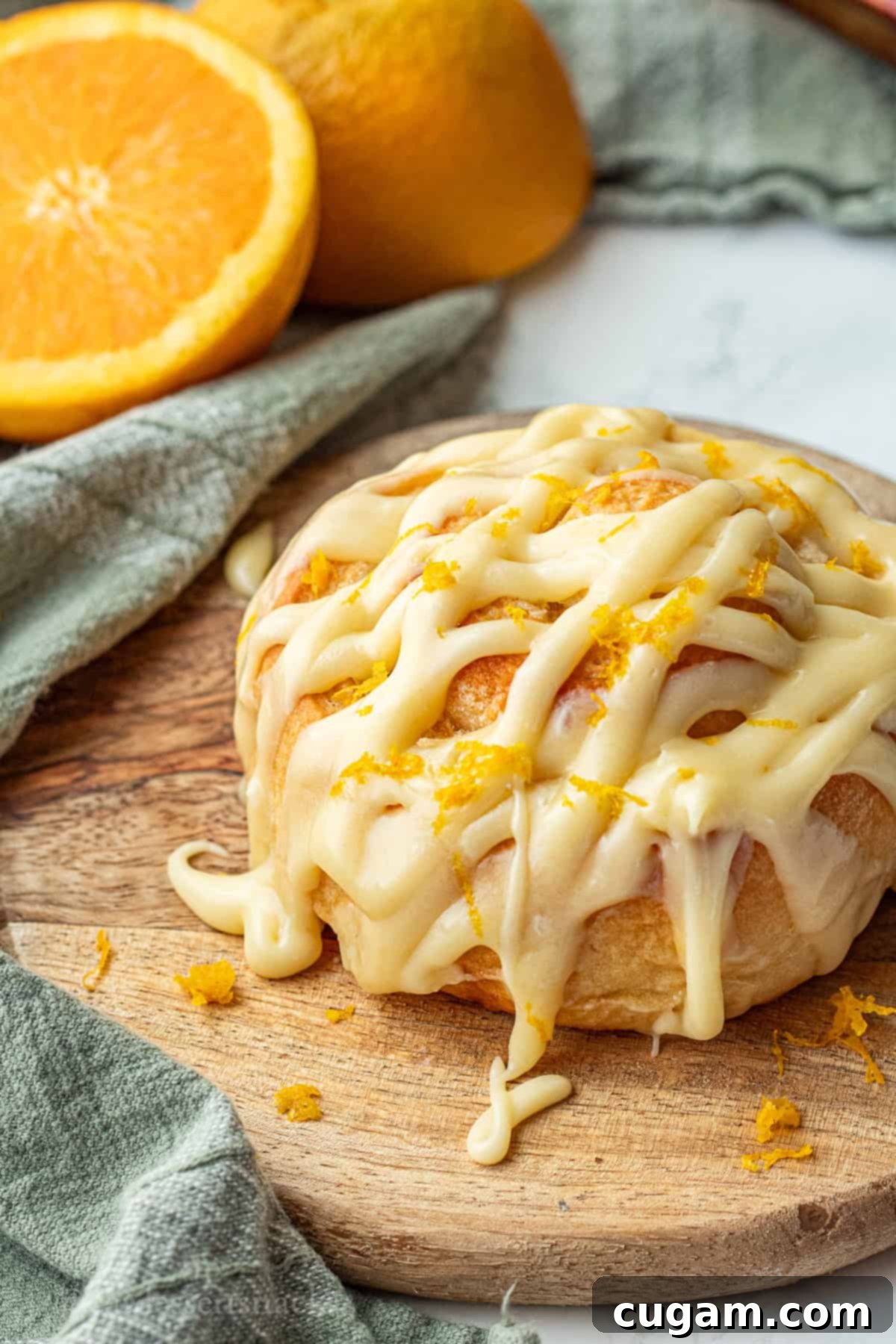 Baked and frosted orange roll on wood cutting board.