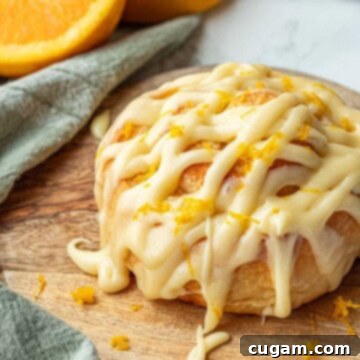 Baked frosted orange roll on wooden cutting board.