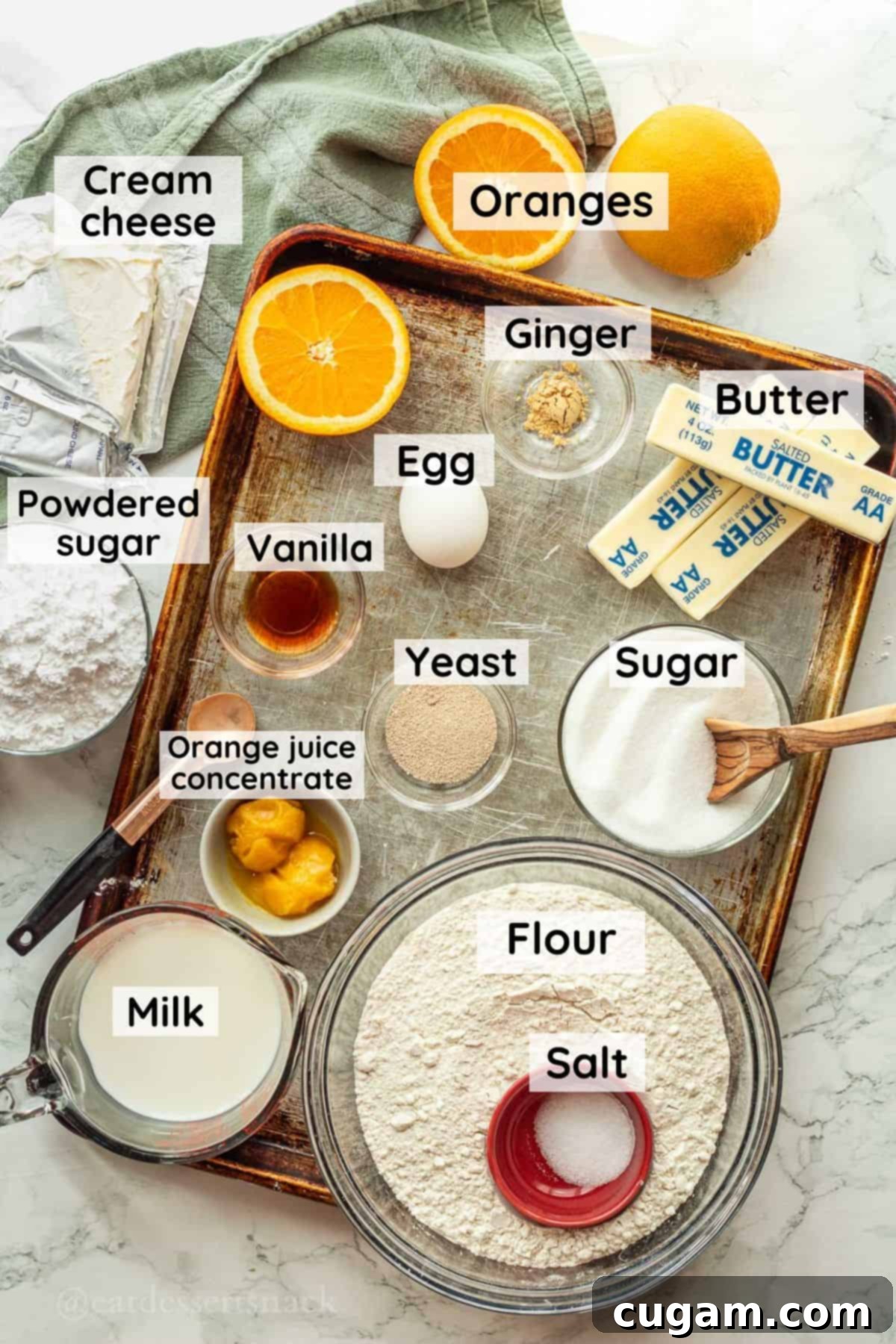 Ingredients for homemade orange rolls in glass bowls on metal baking sheet with green dish towel.