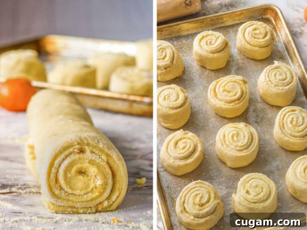 Raw orange roll dough in a spiral with orange zest and sugar inside on marble countertop, and raw orange rolls on baking sheet.