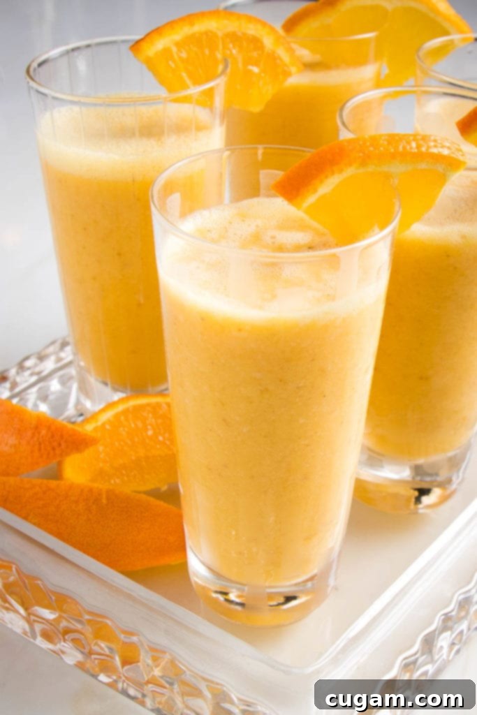 Creamy Orange Bliss 2 A tall glass filled with a frothy, vibrant orange smoothie, garnished with a fresh orange wedge. The texture appears smooth yet thick, inviting a refreshing sip.