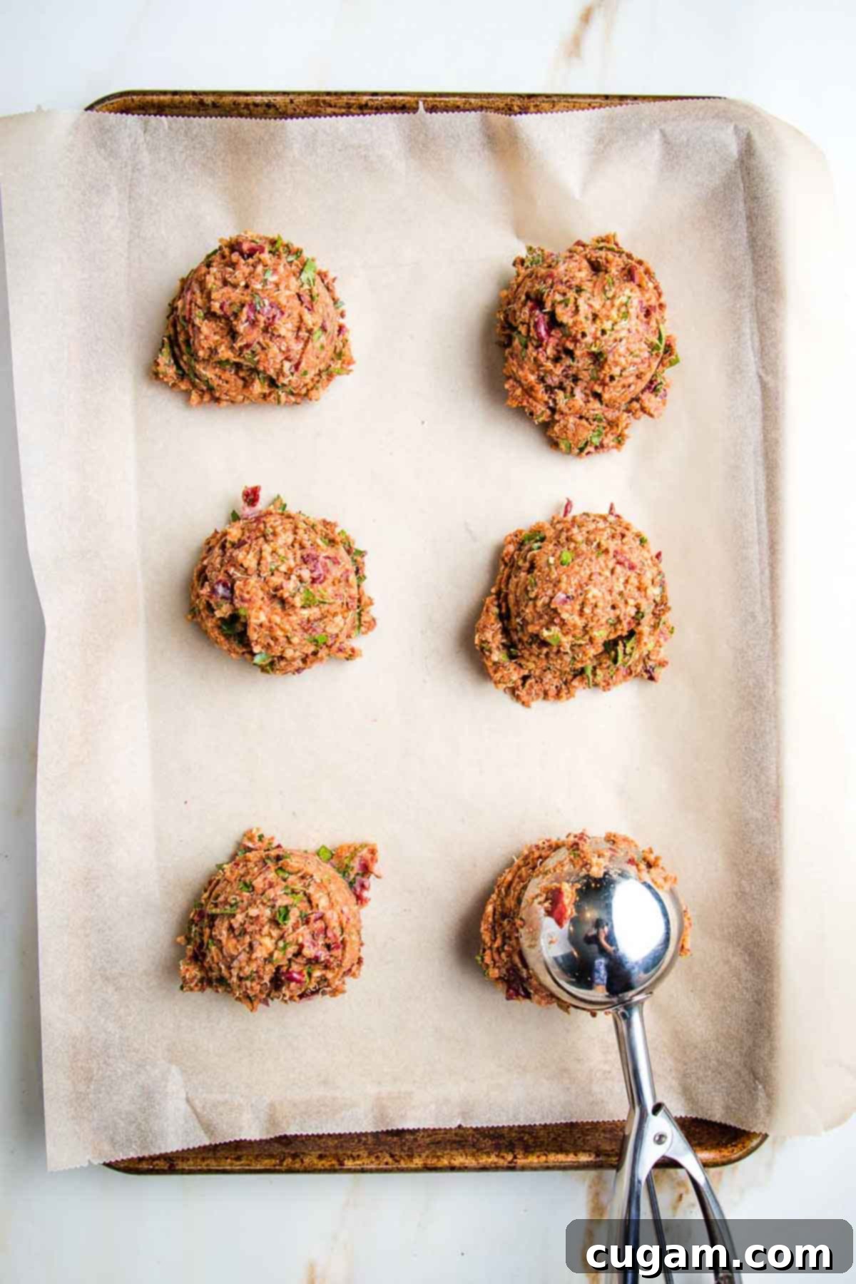 Portioning out veggie burger mixture onto a parchment-lined baking sheet using a large scooper for even sizing.