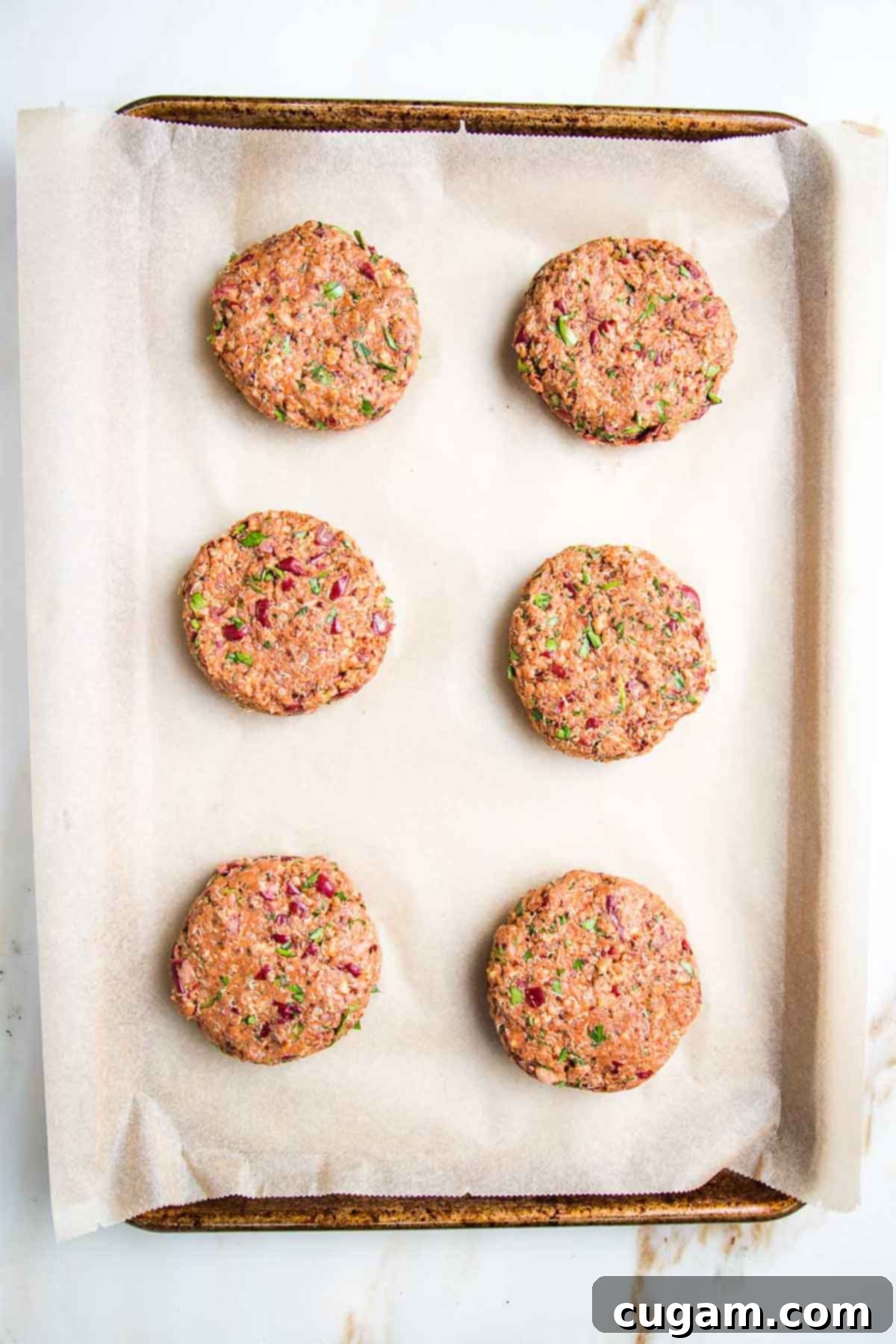Six perfectly formed veggie burger patties arranged on a parchment-lined baking sheet, ready for cooking.