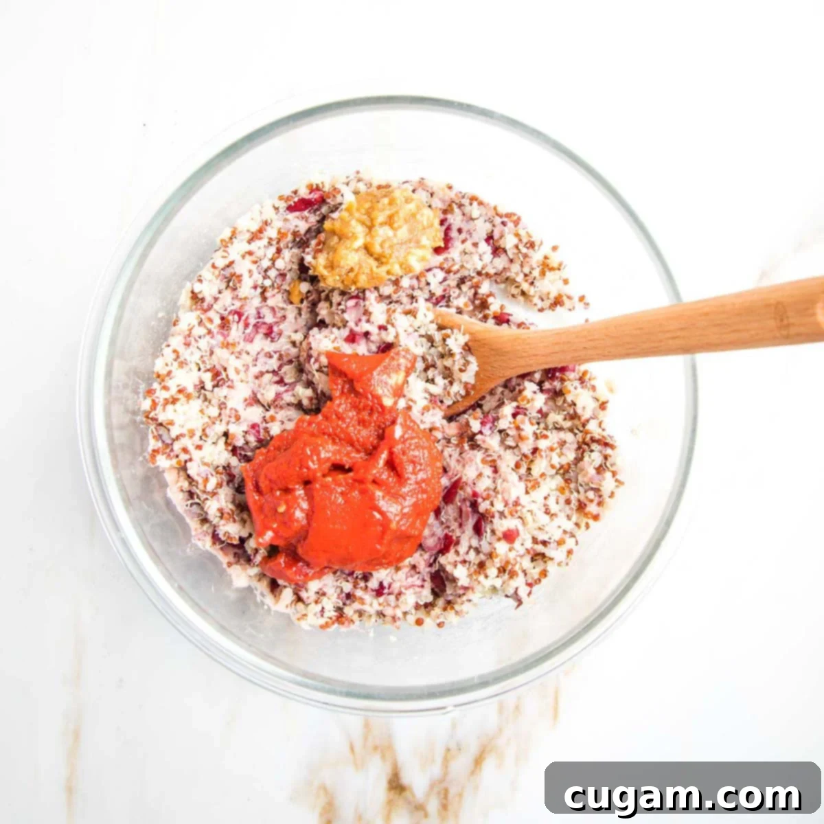 Tomato paste and miso paste added on top of a mixture of quinoa and mashed beans, ready to be incorporated.