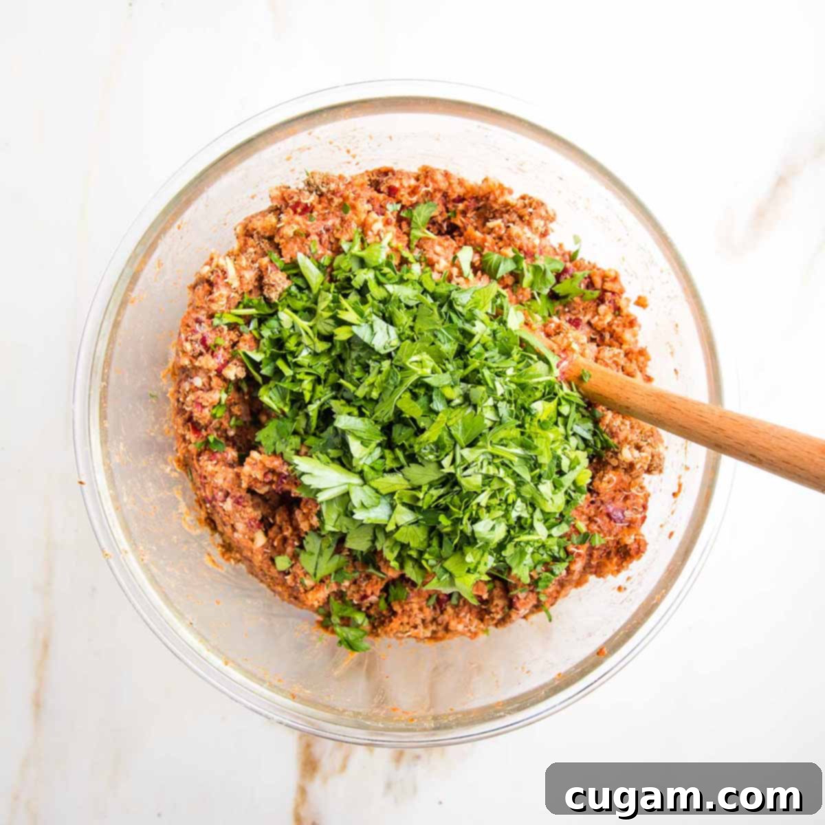 Freshly chopped parsley generously sprinkled on top of a vibrant veggie burger mixture in a glass bowl.