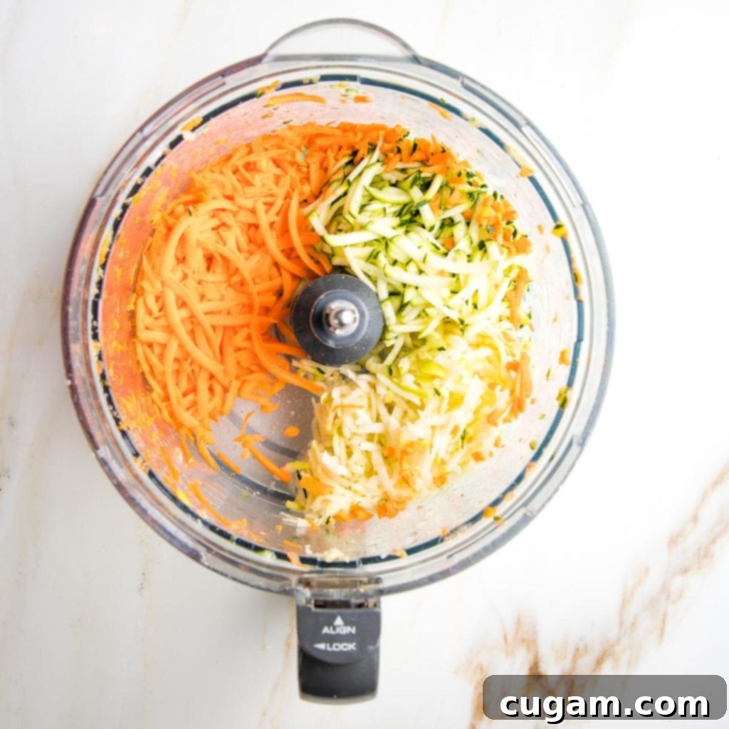 Bowl of shredded vegetables next to a box grater, ready for muffin making.