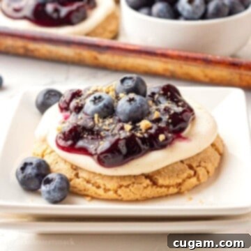 Blueberry pie filling on top of cheesecake cookie on white plate.